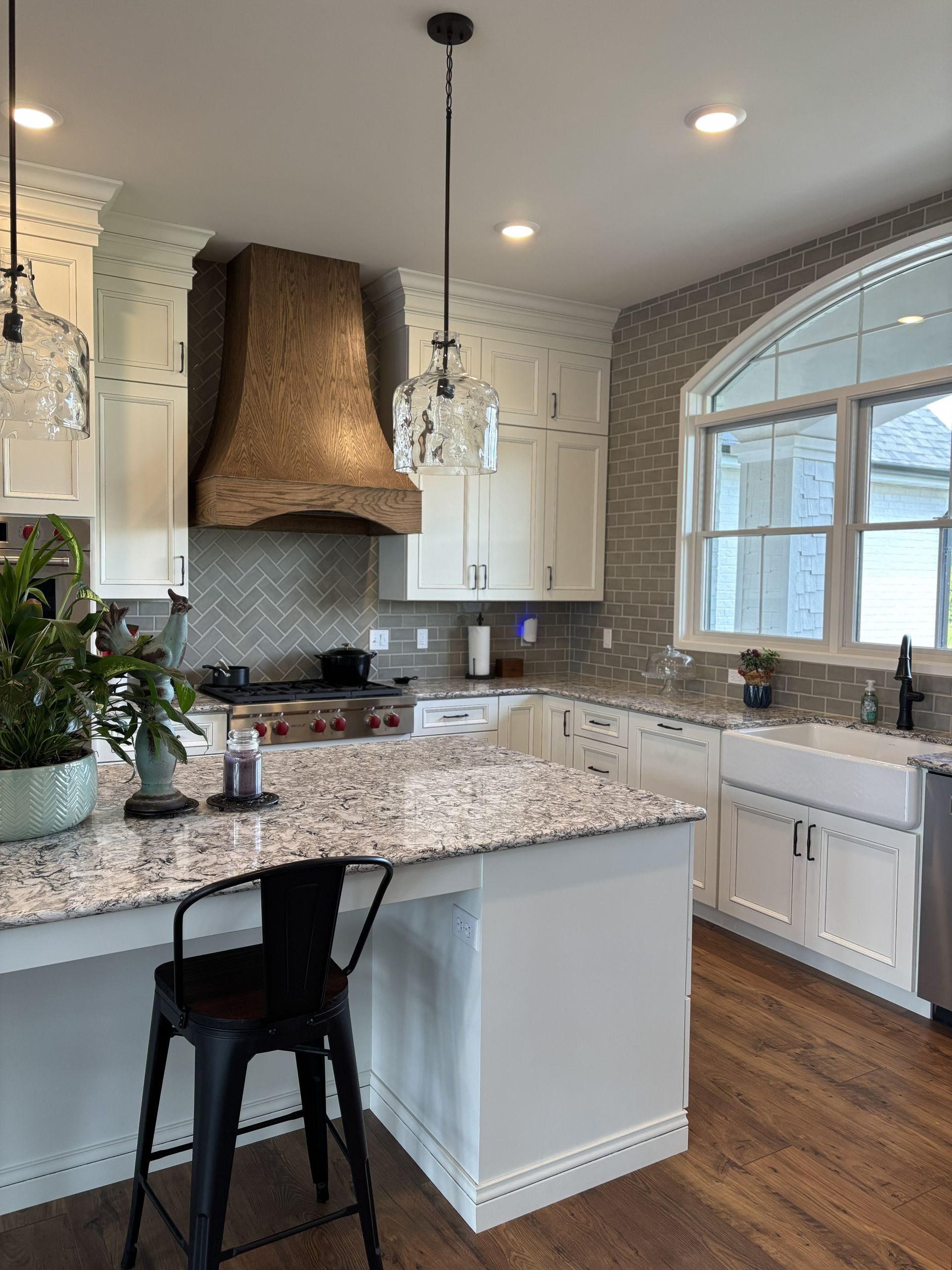 Kitchen with white cabinets, wood hood, and a granite countertop island with a black stool.