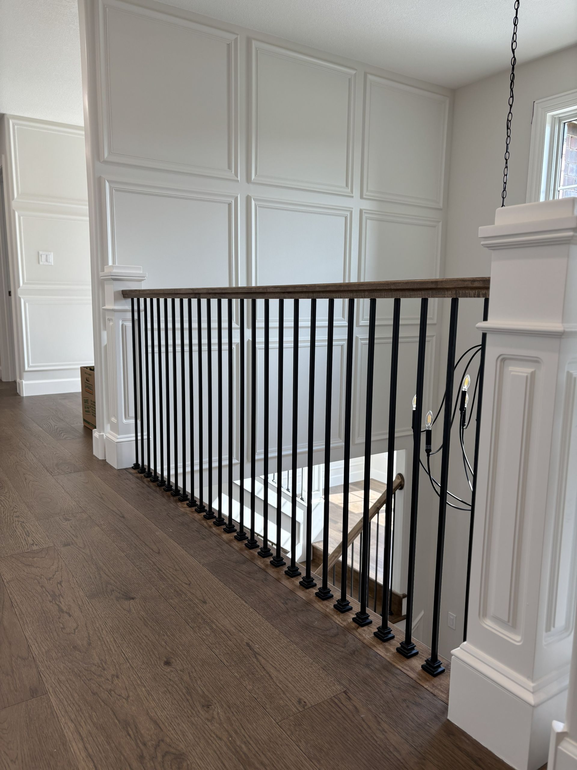 Hallway with wood floor, white paneled wall, black railing, and staircase.