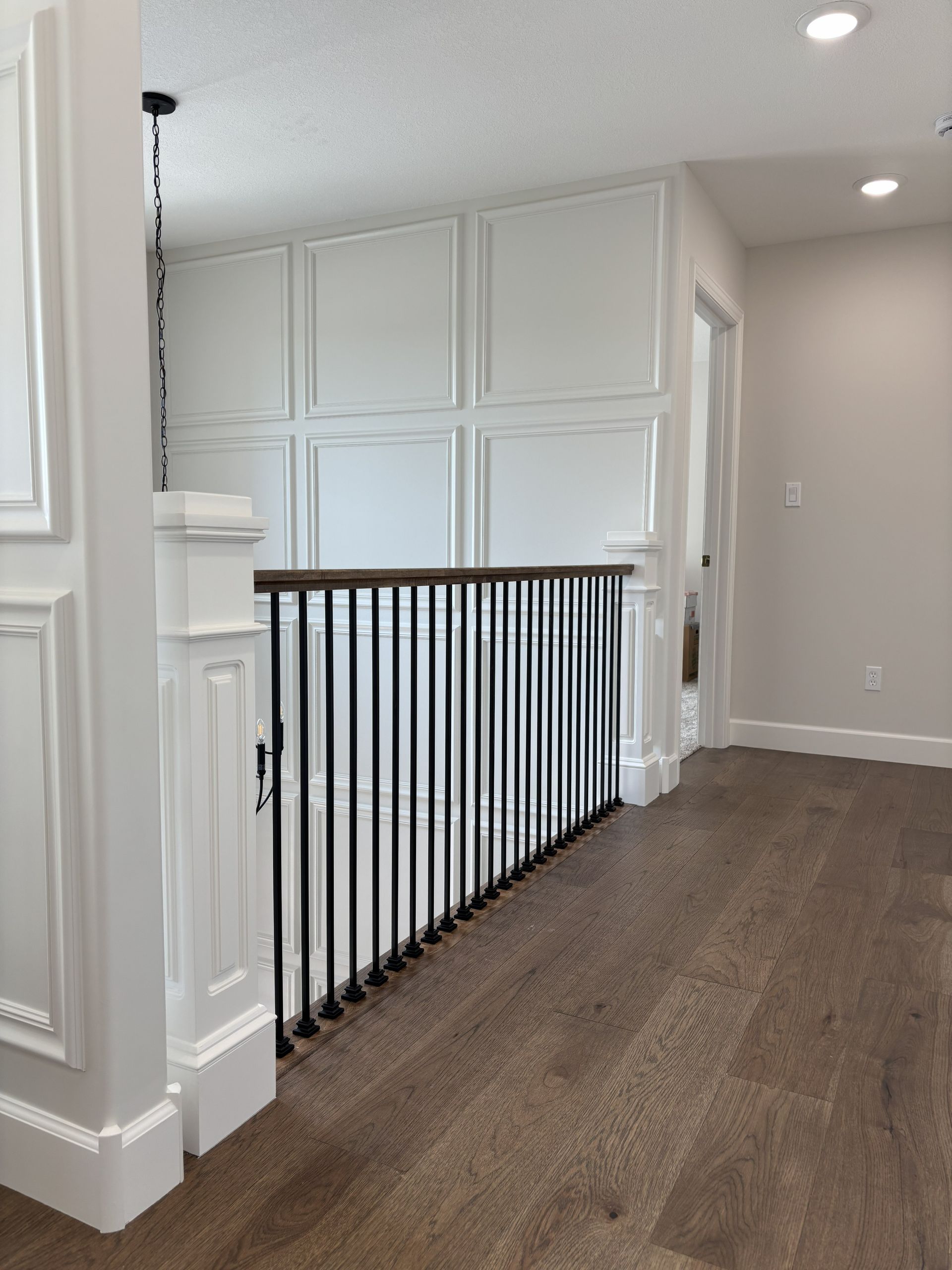 Hallway with wood floor and black railing, white wall paneling.