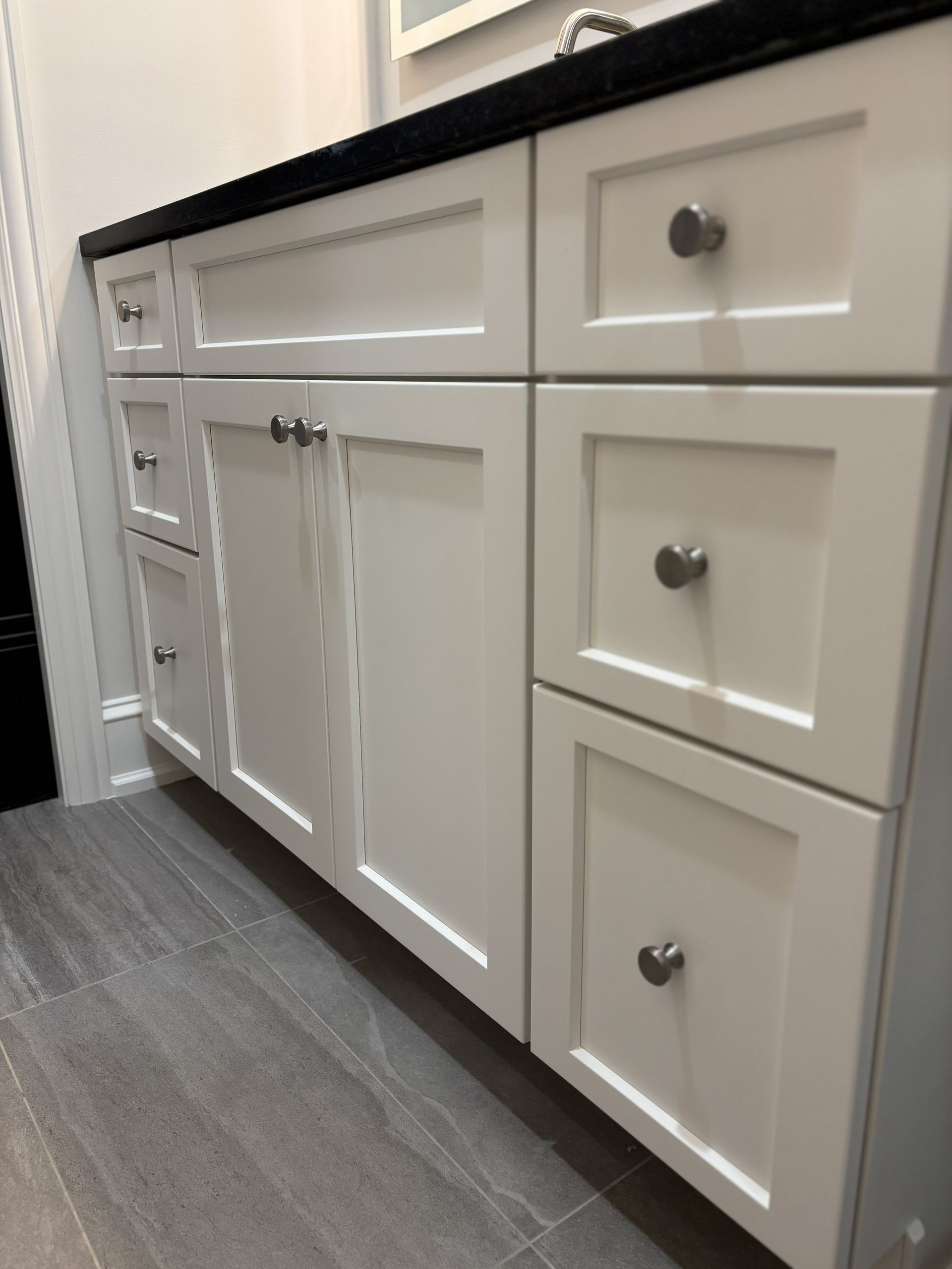 White bathroom vanity with black countertop and silver hardware.