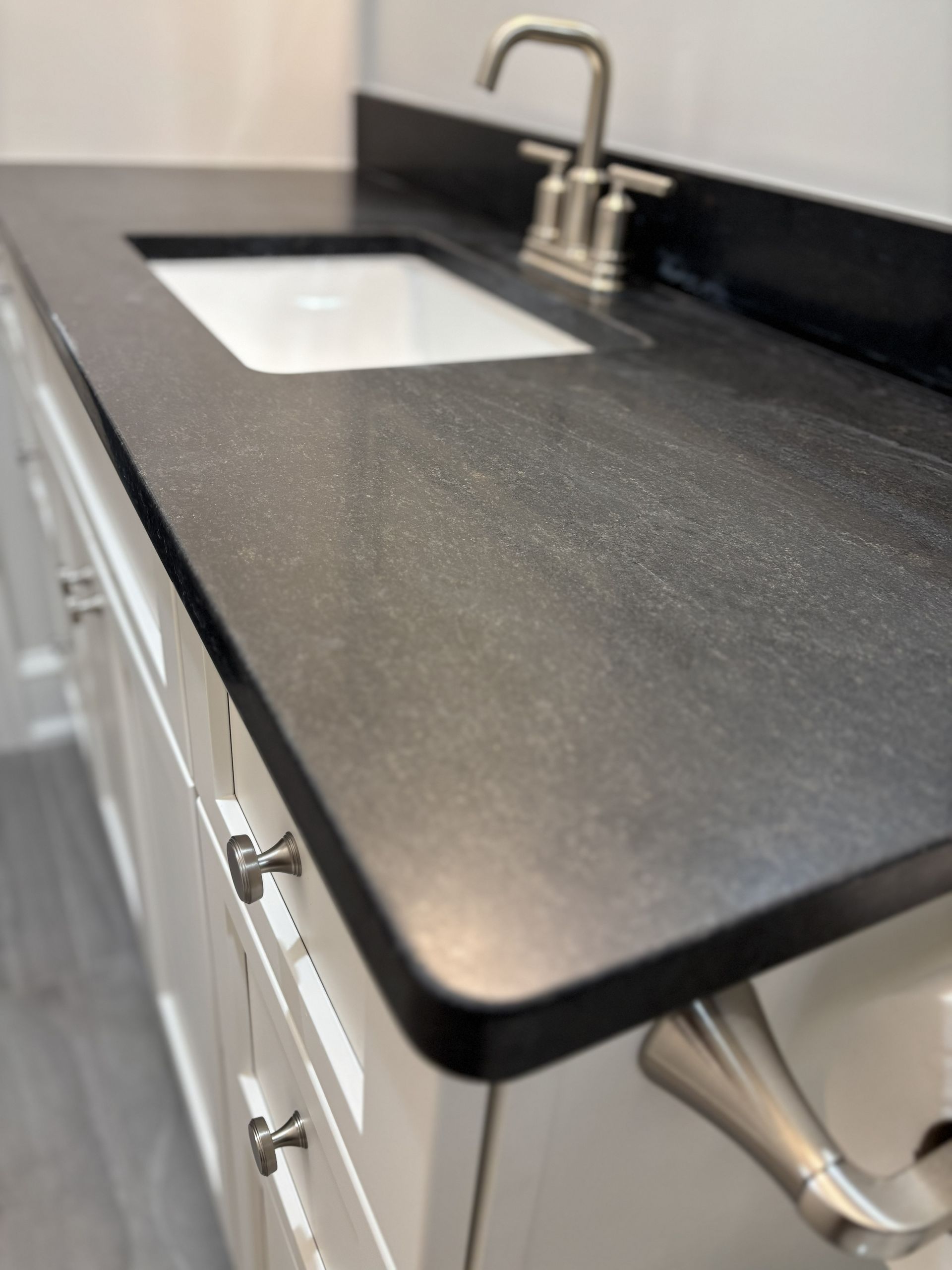 Bathroom vanity with black countertop and white cabinets, silver faucet and sink.