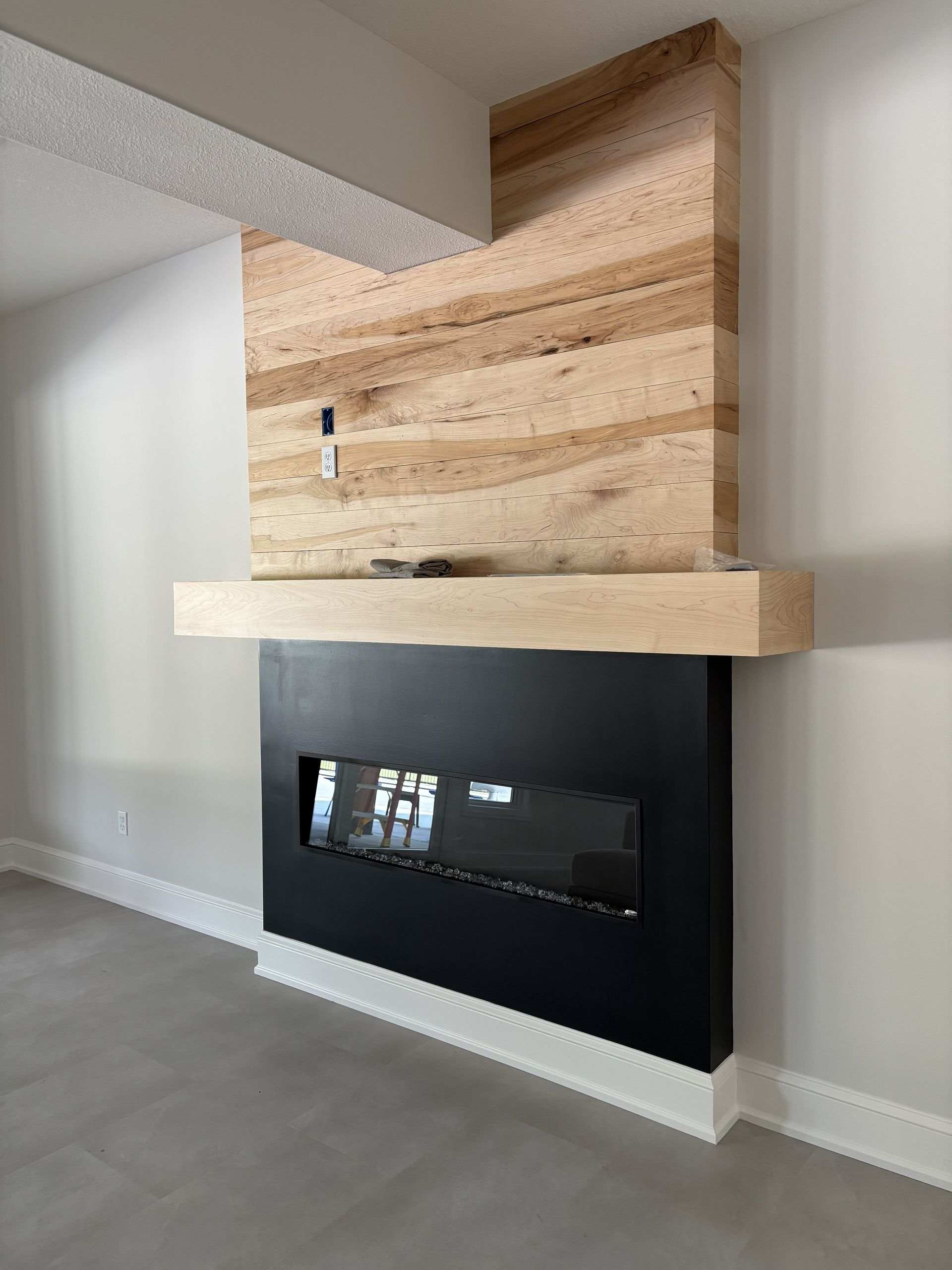Modern fireplace with layered wood surround, black frame, and glass insert. Beige, gray and black tones.