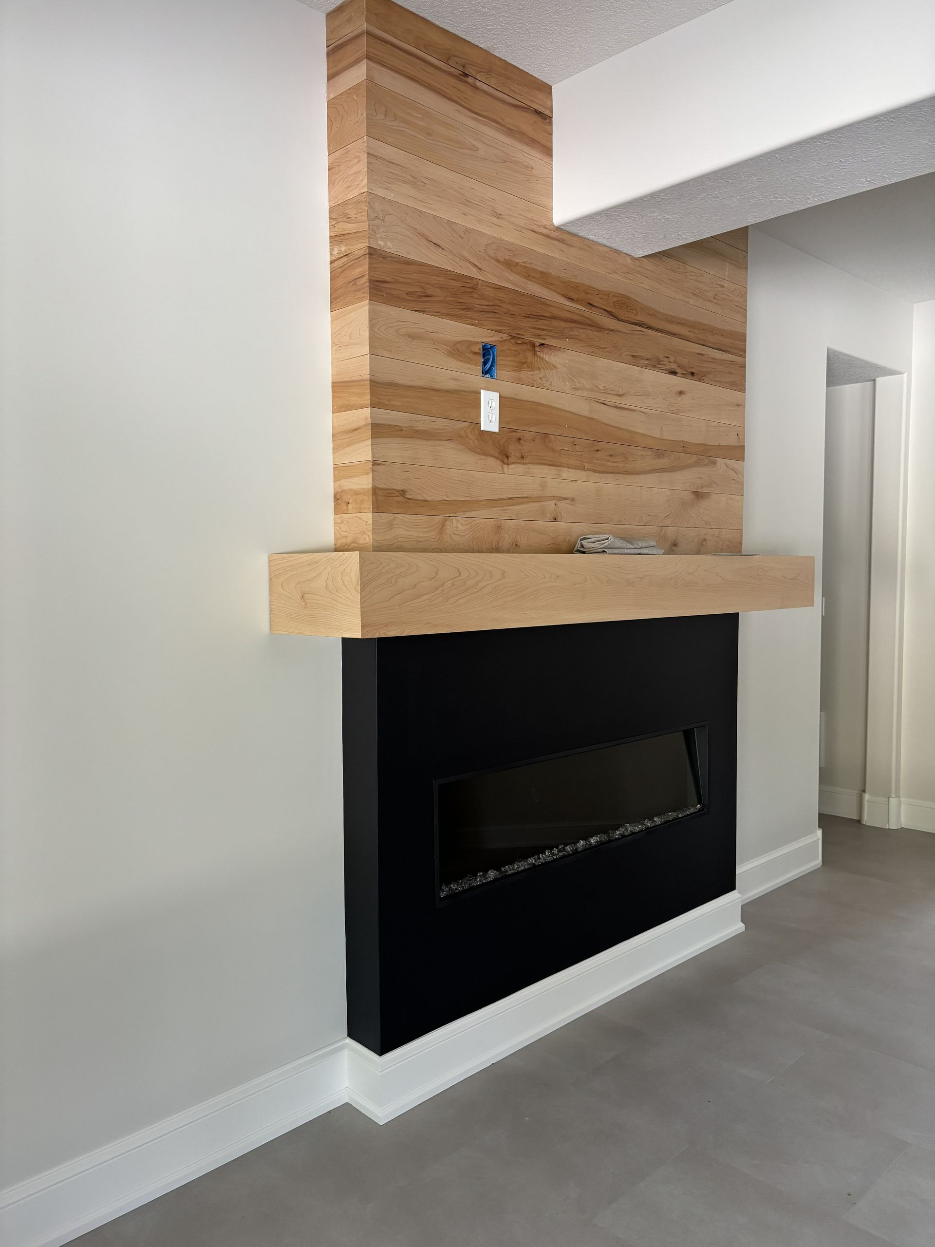 Modern fireplace with black surround, wooden mantel, and textured wall detail.