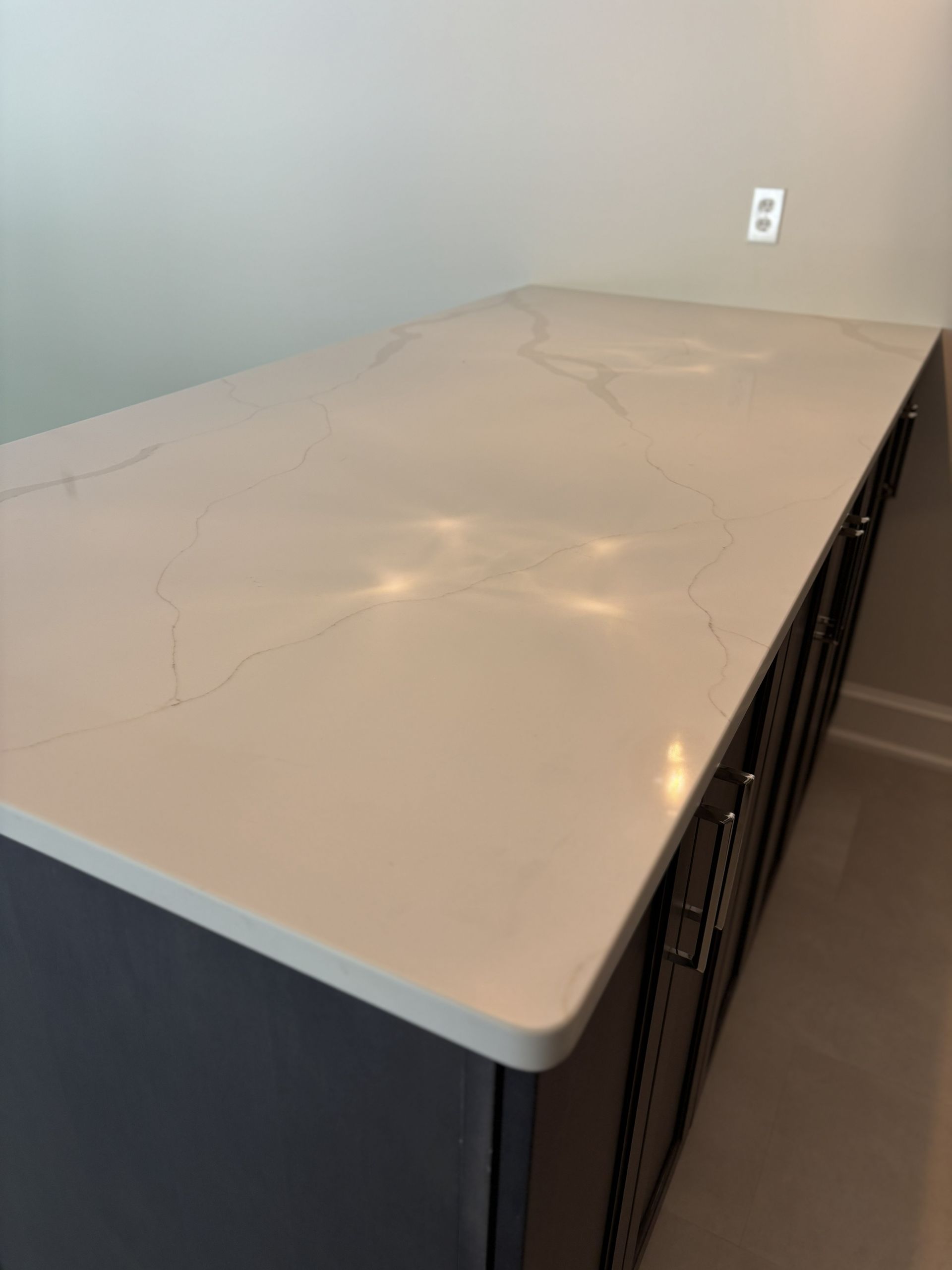 A light-colored countertop with subtle veining rests on a dark cabinet. Wall and outlet visible.