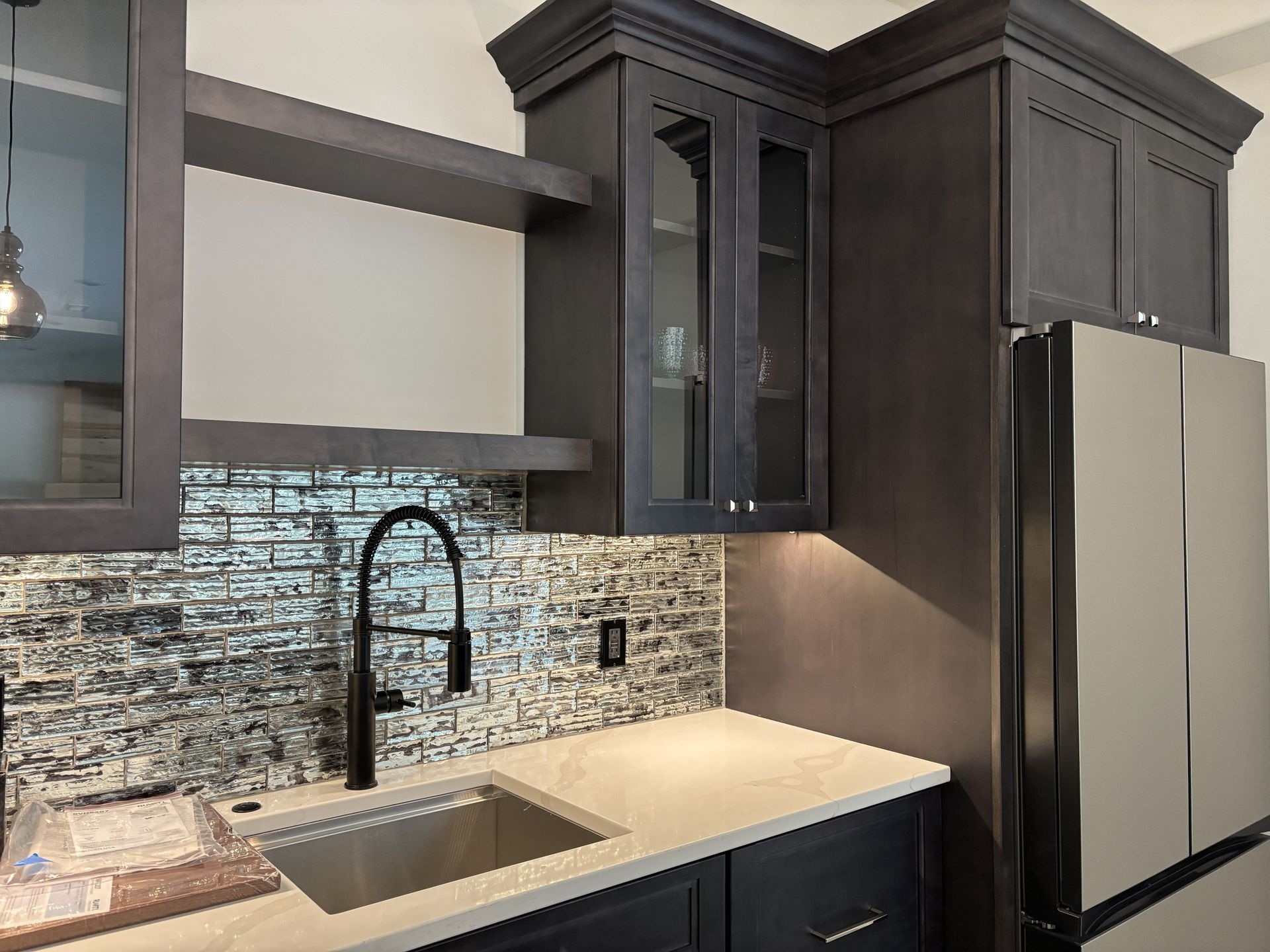 Dark wood cabinetry with a sink, backsplash, and refrigerator in a kitchen setting.