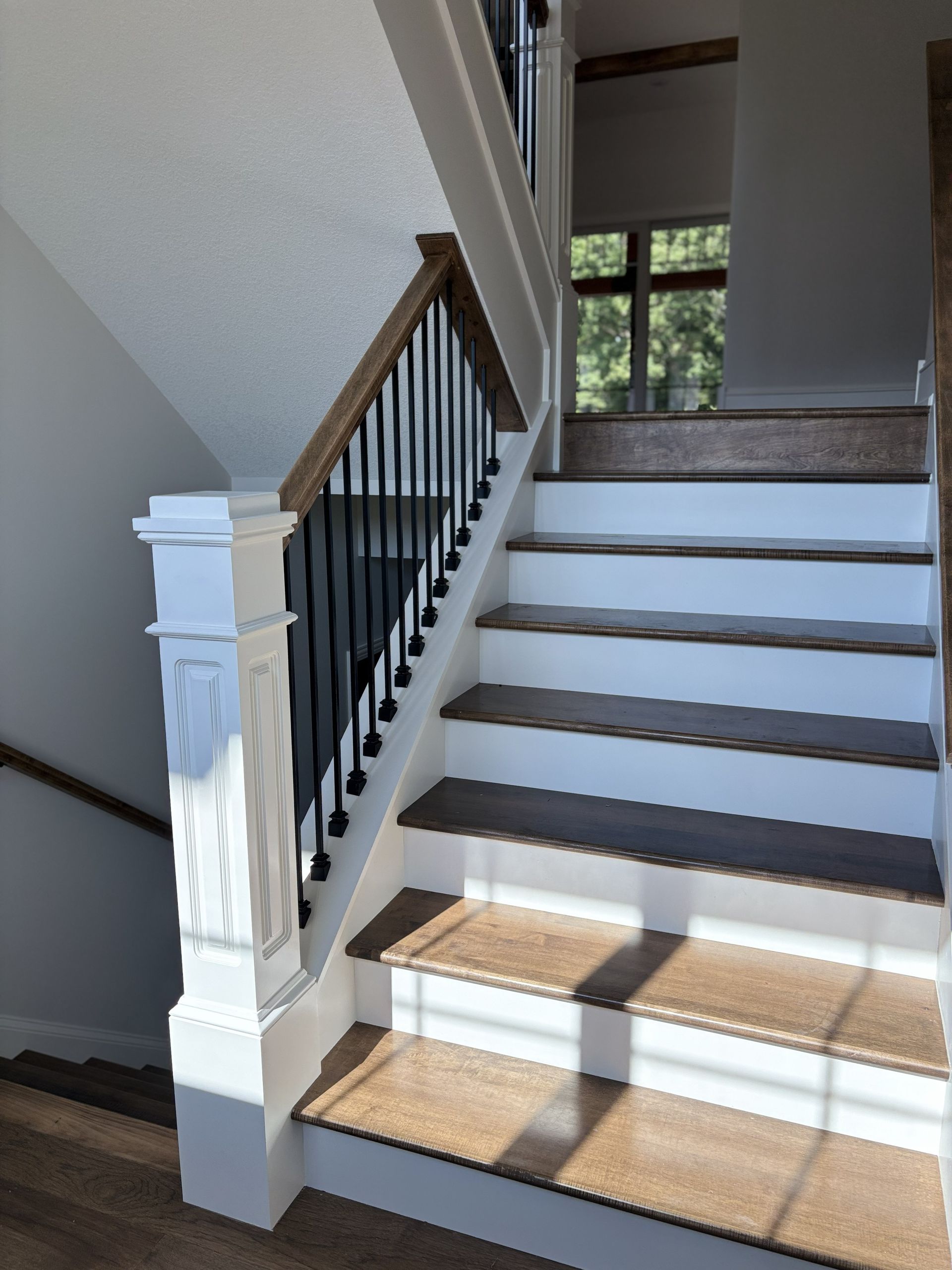 Staircase with wood treads and white risers, black spindles and wood handrail, white newel post, and window at top.
