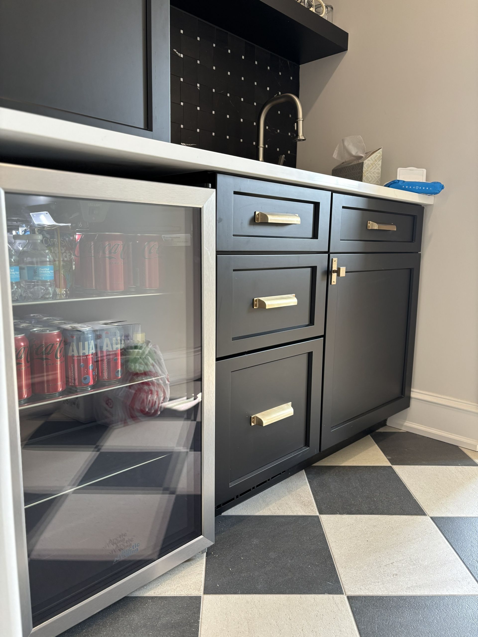 Built-in wet bar with black cabinets, white countertop, and drink cooler on checkered floor.