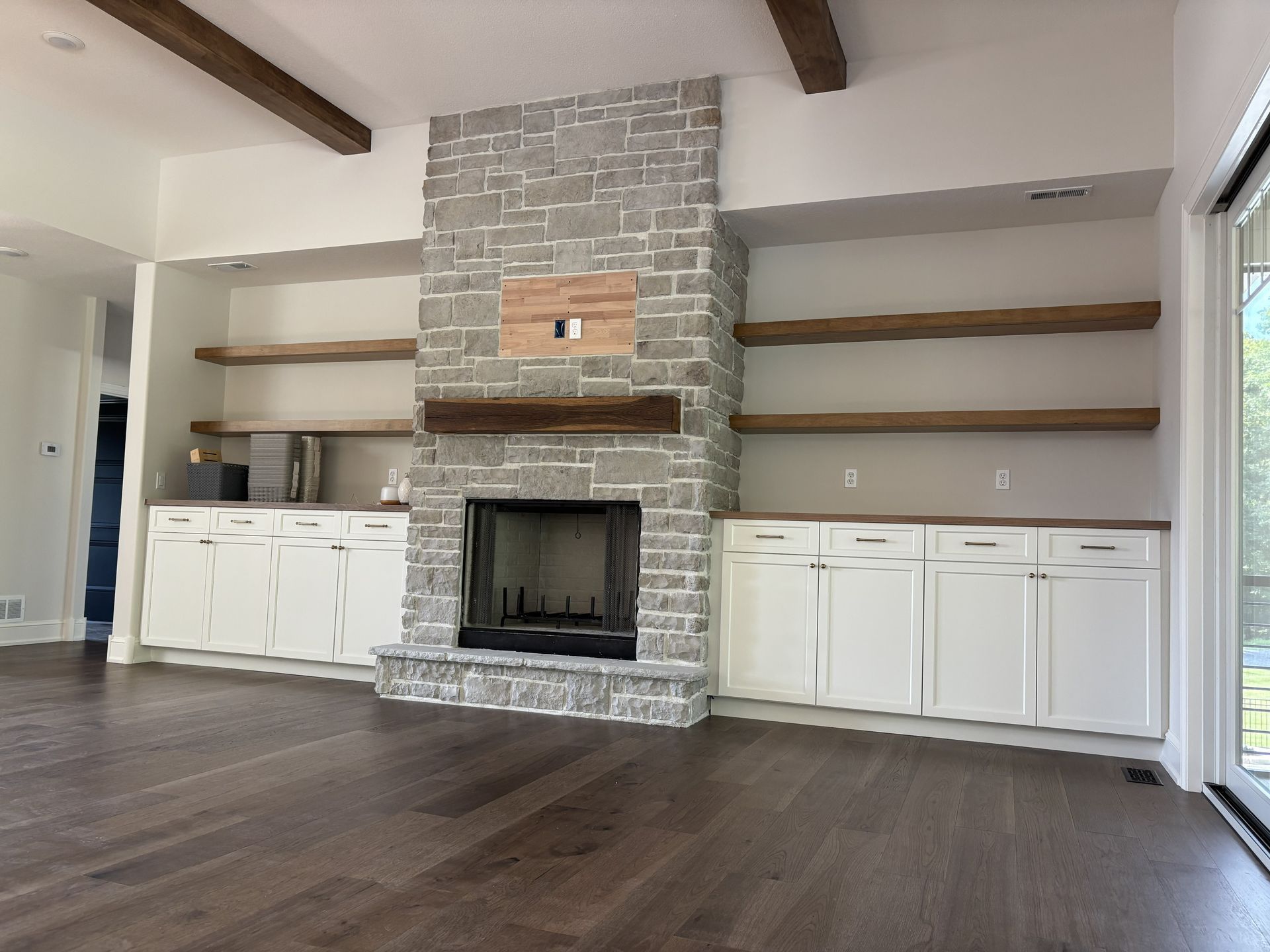 Living room with stone fireplace, built-in shelves, white cabinets, and dark wood floors.