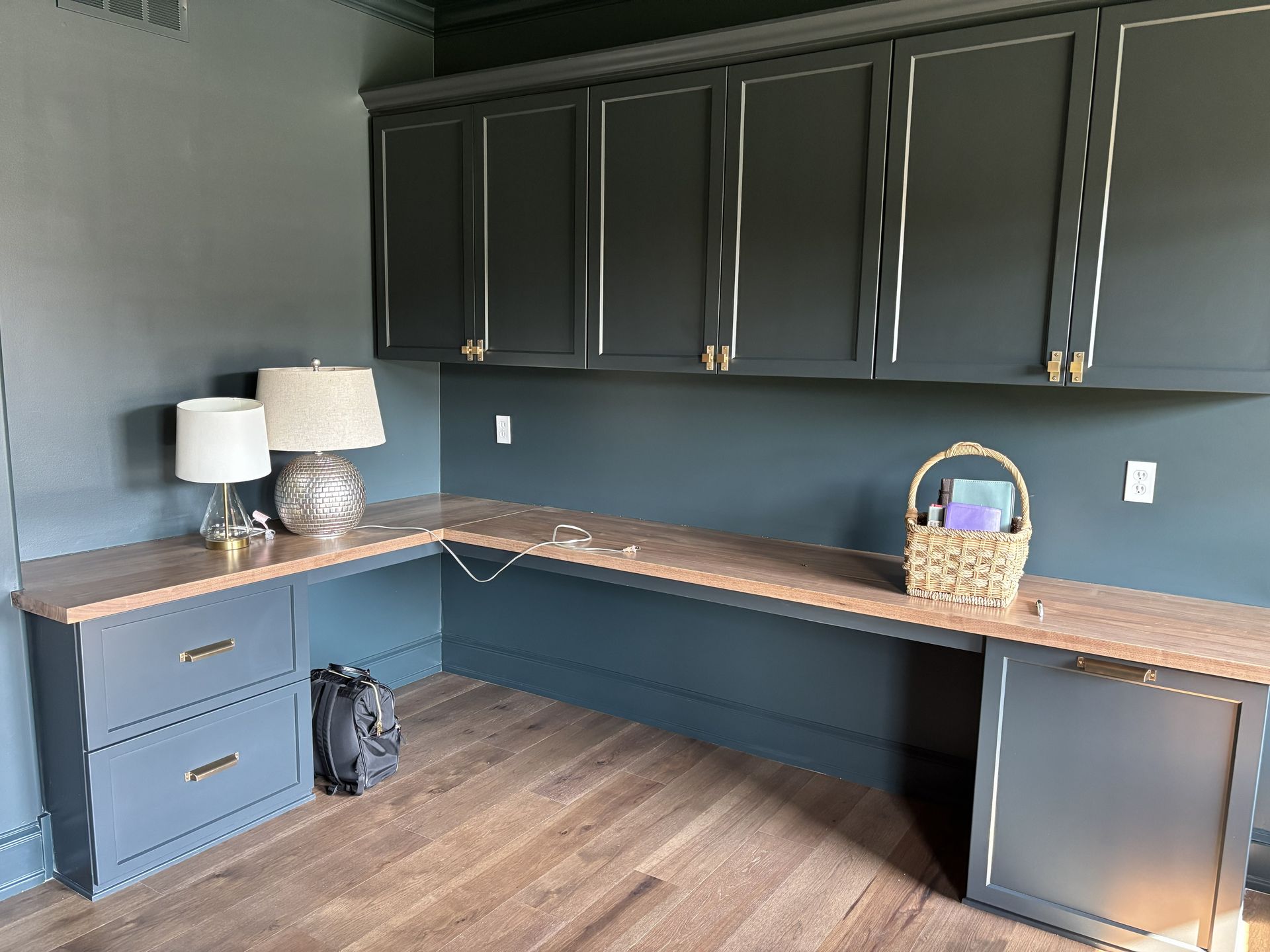 Dark blue office with wooden desk, cabinets, lamps and basket.