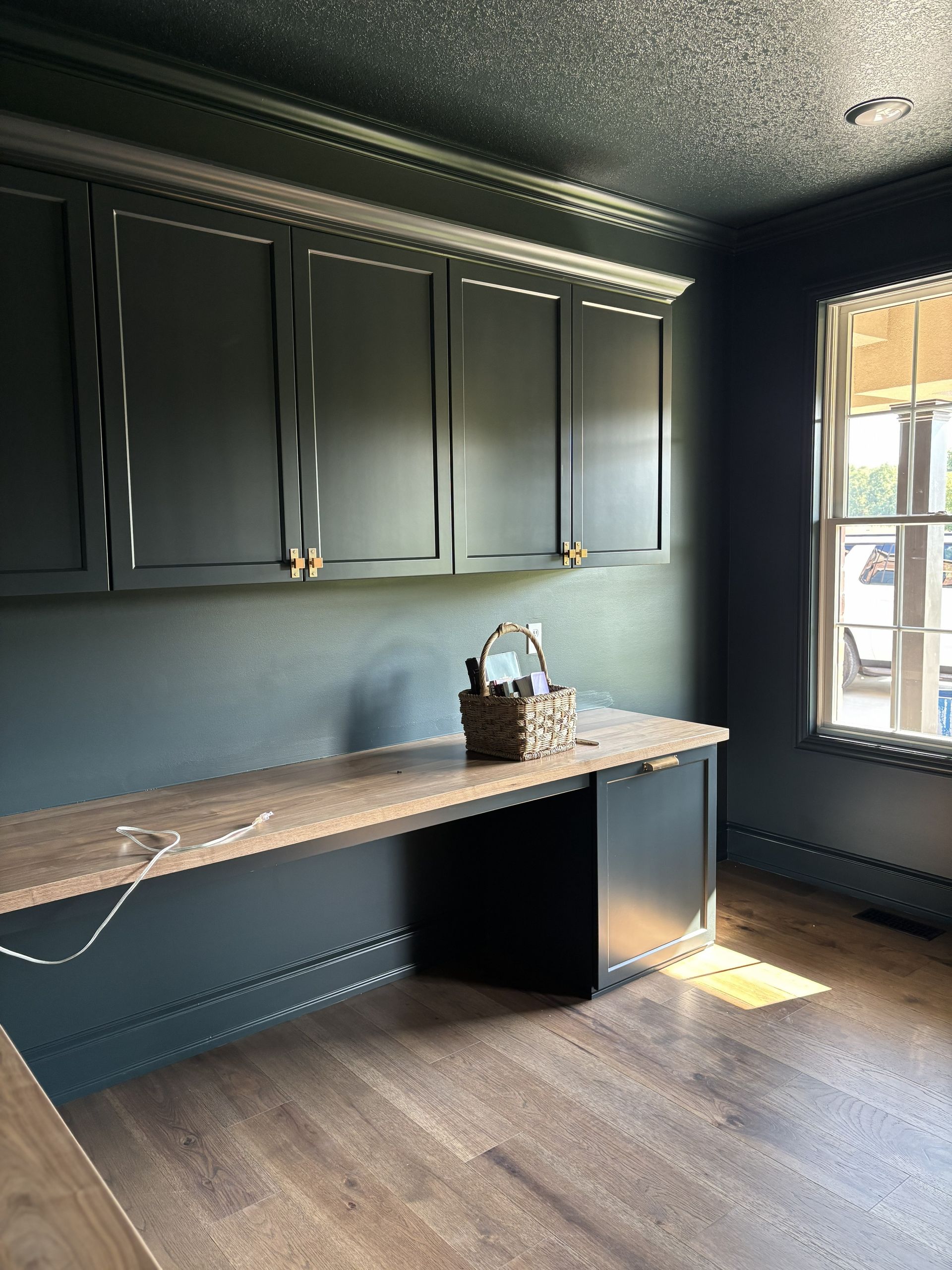 Dark blue office with wooden desk and cabinets, a window, and a basket.