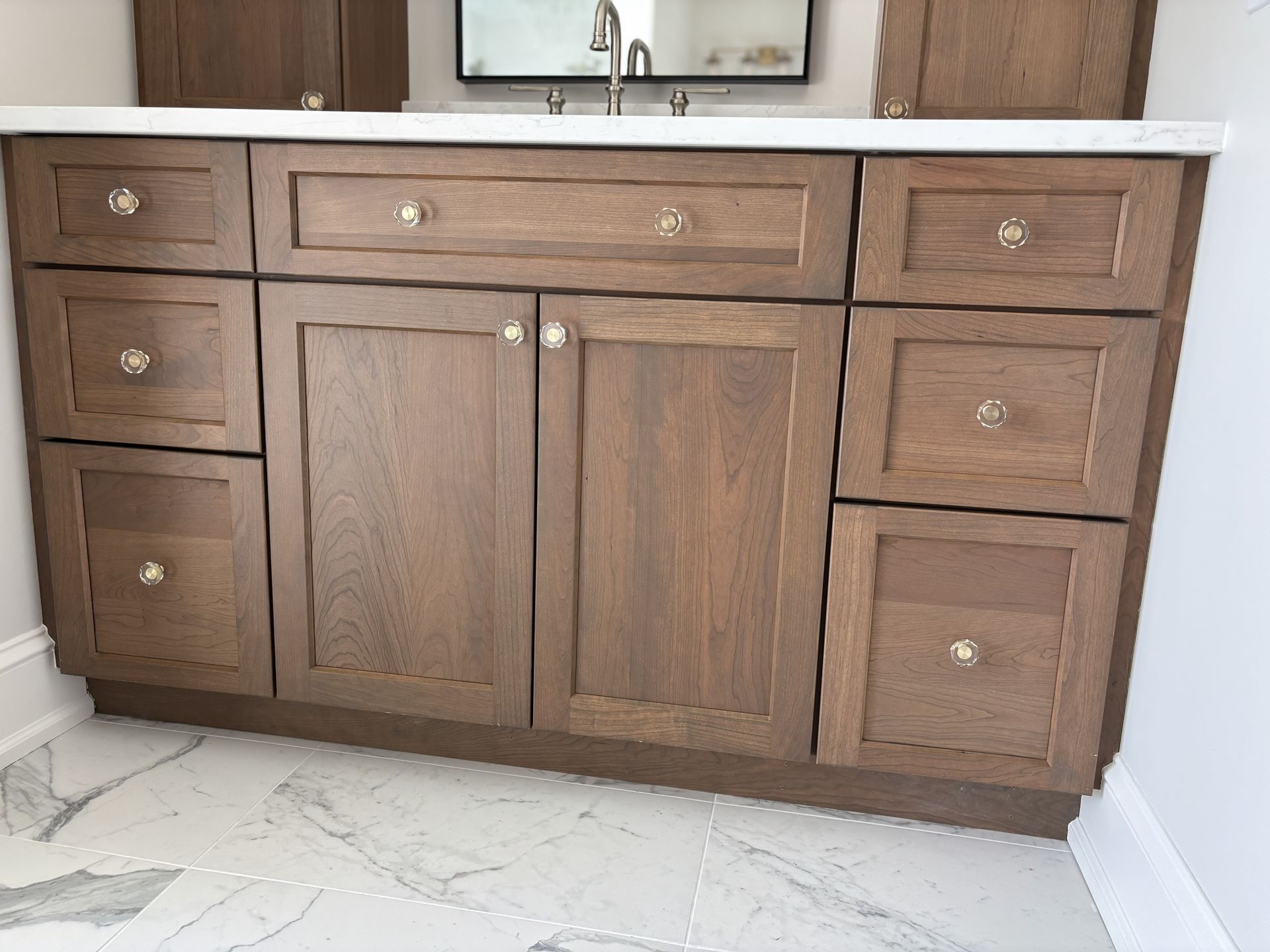 Bathroom vanity with brown cabinets, white countertop, and crystal knobs.