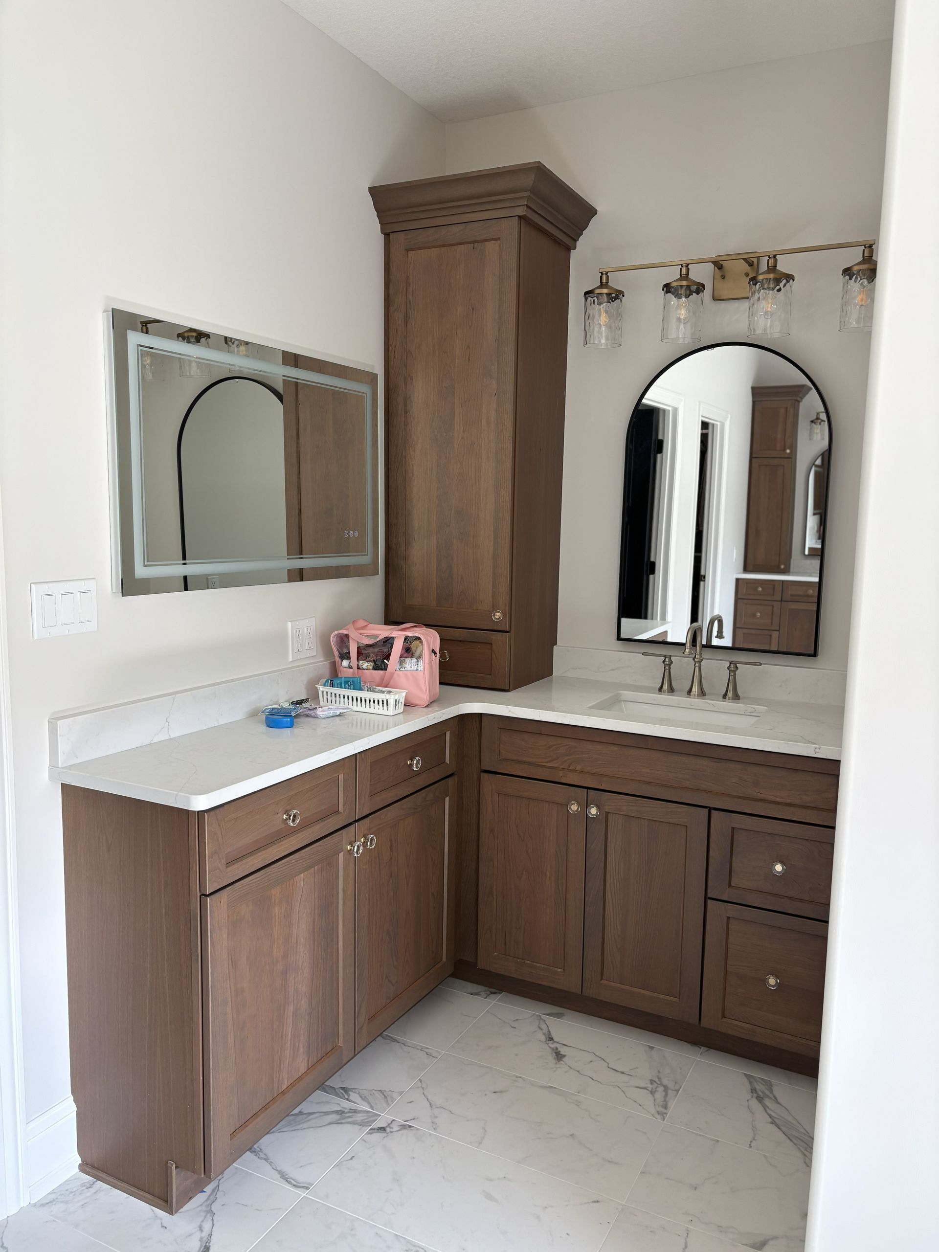 Bathroom with brown cabinets, white countertop, two mirrors, and a tall cabinet.