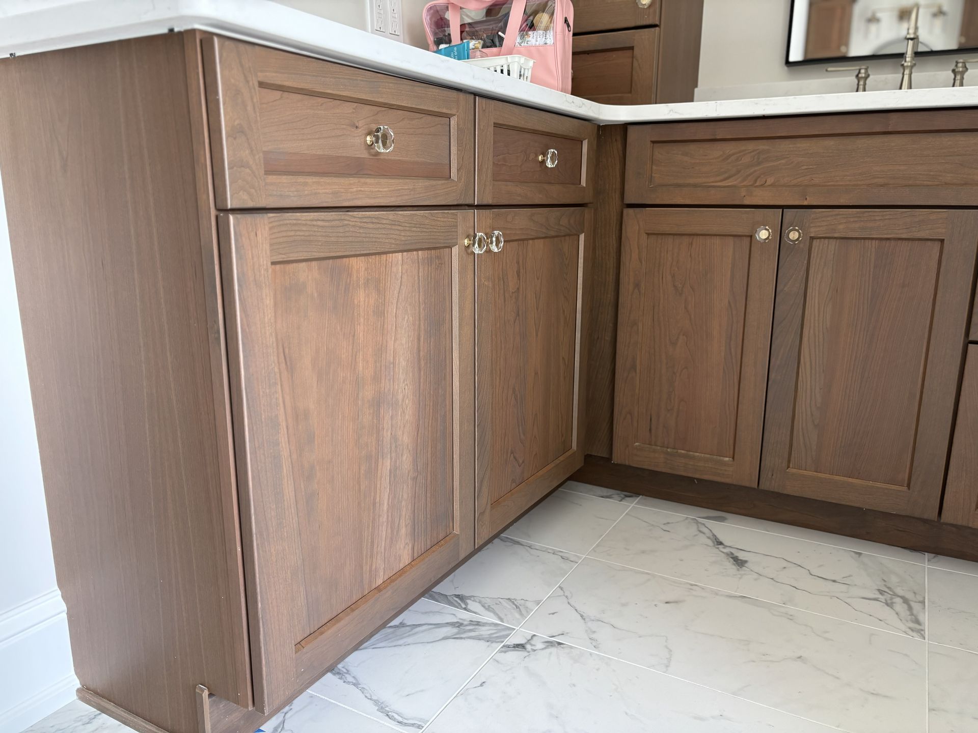 Brown wooden bathroom vanity with two doors and two drawers on a marble-tiled floor.