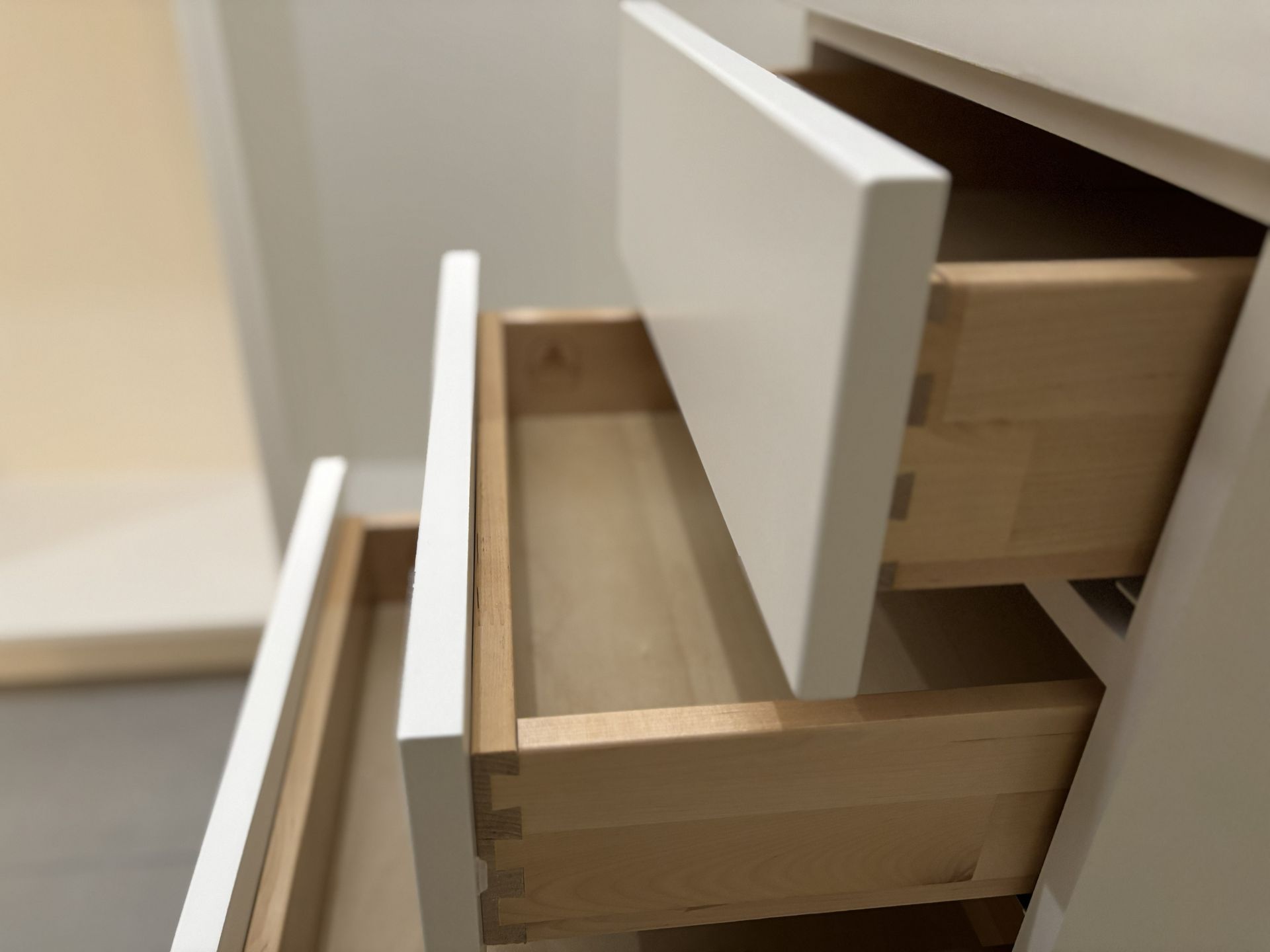 Open, empty wooden drawers with white fronts in a cabinet.