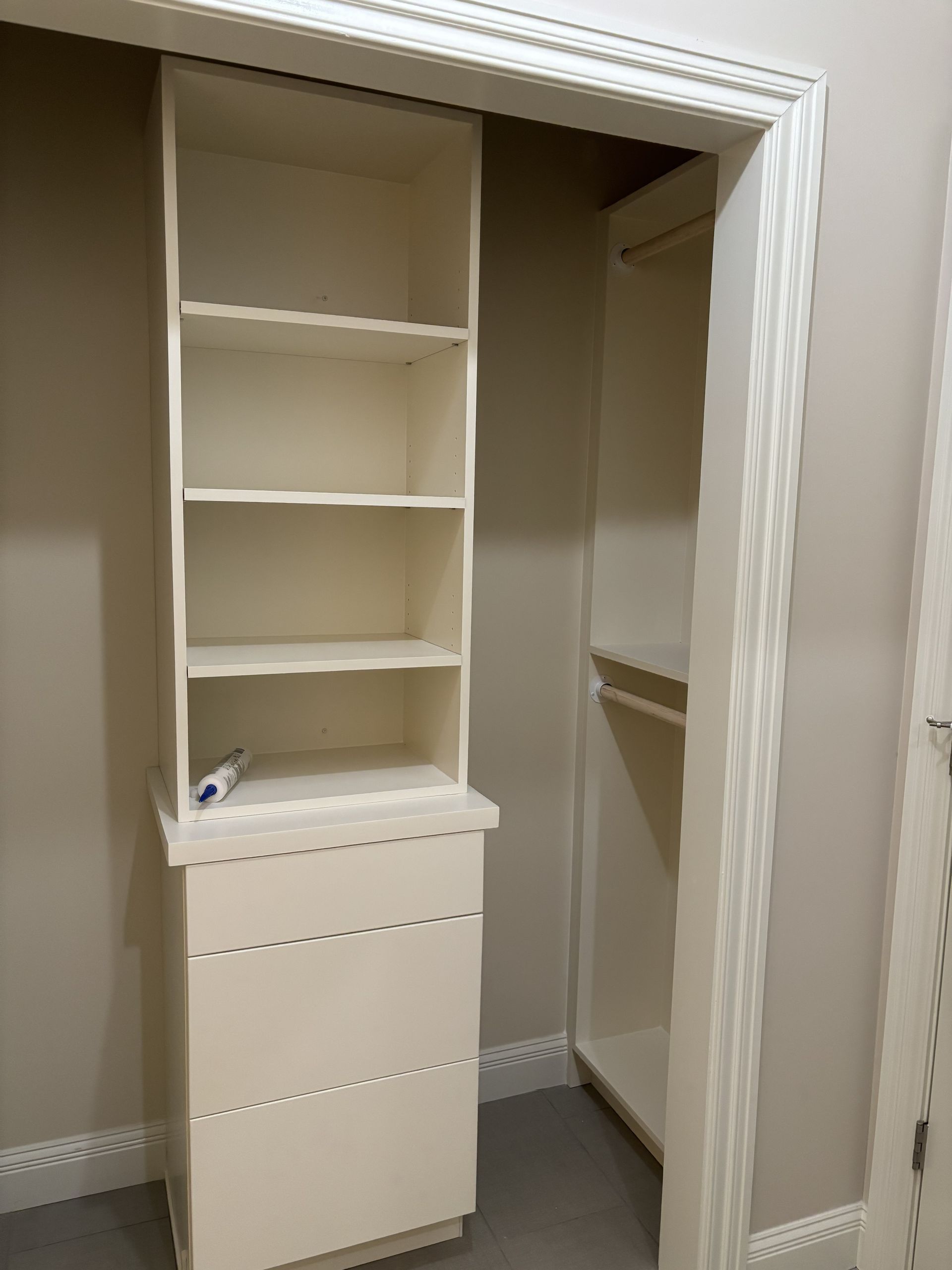 Built-in closet with shelves and drawers. Off-white cabinets and walls. Closet door frame on the right.