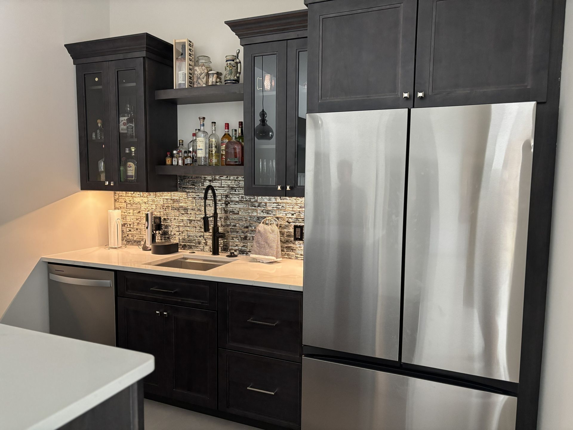 Dark gray home bar with stainless steel fridge, sink, and liquor display.