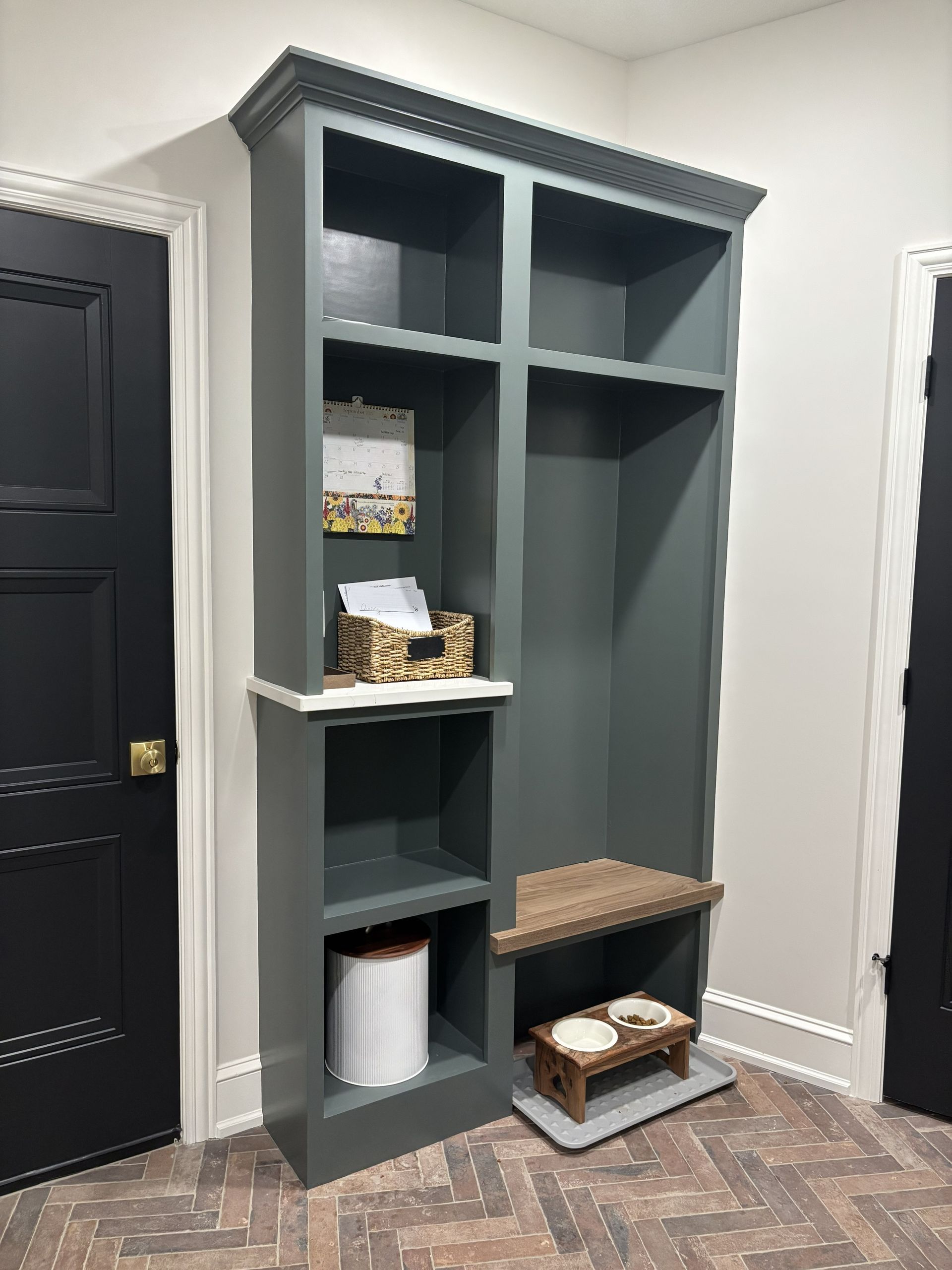 Tall, dark green built-in shelving unit with open shelves, decorative molding, and a small built-in dog step.