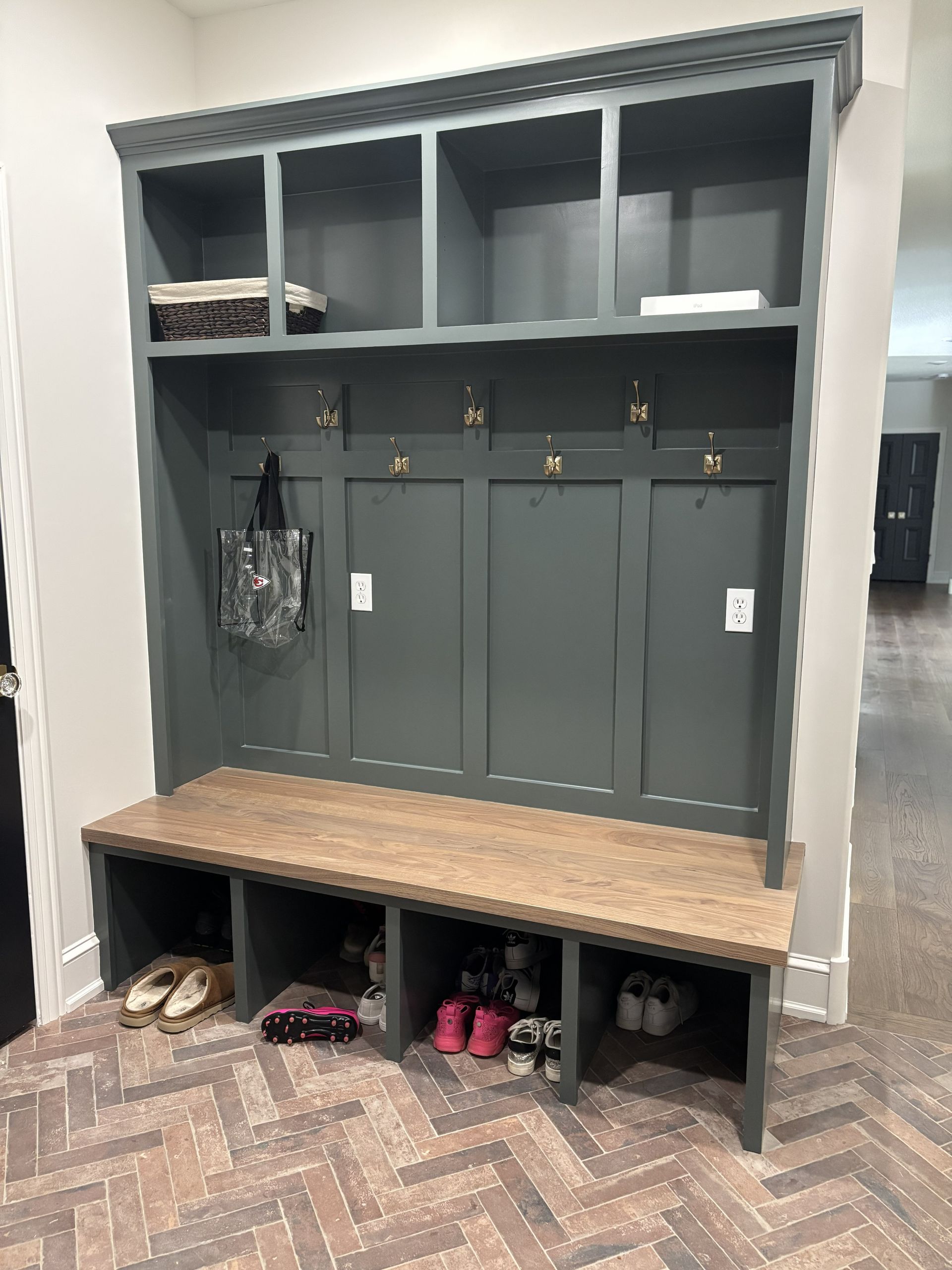 Gray mudroom storage unit with hooks, bench, and shoe cubbies.