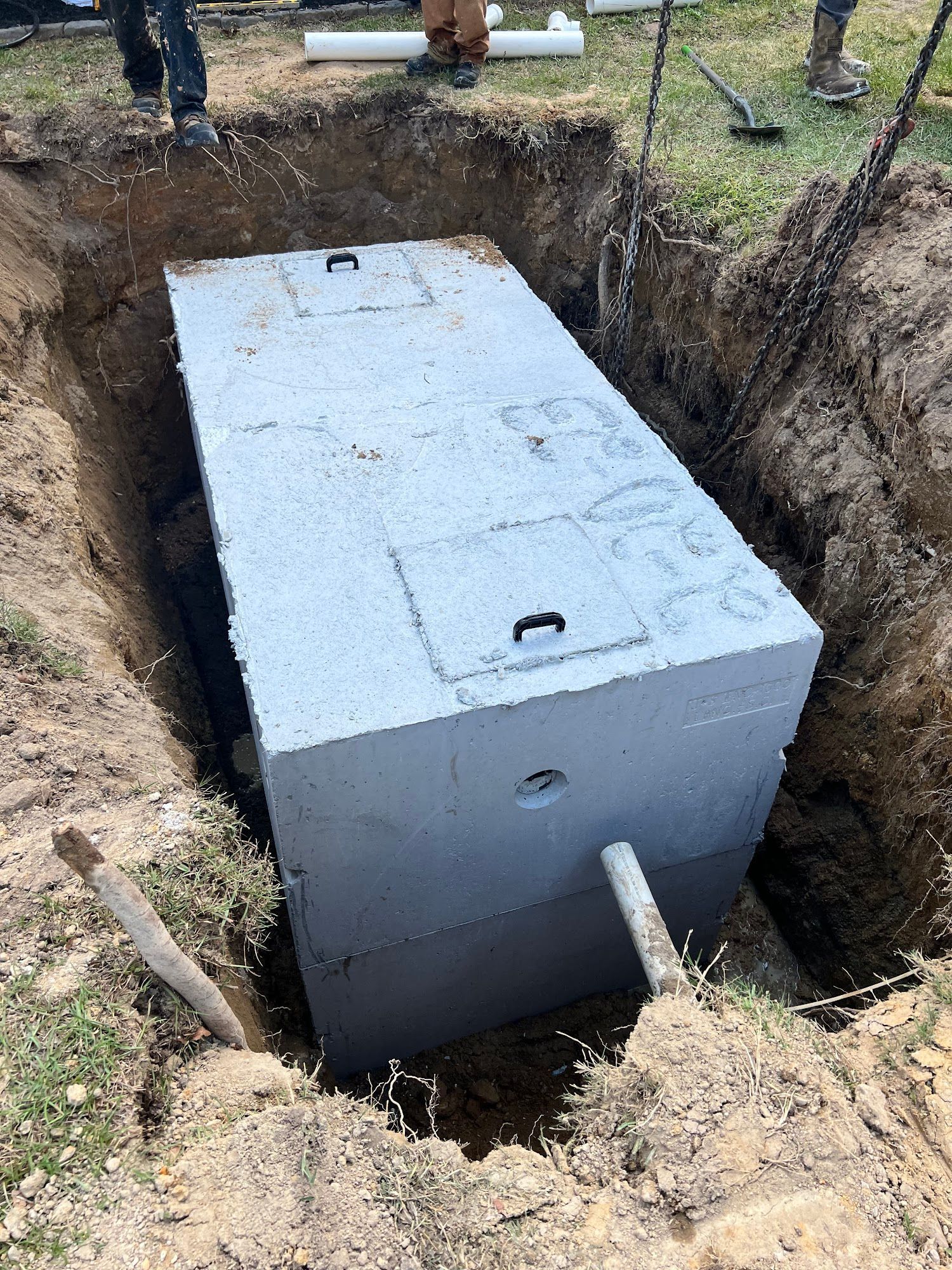 A large concrete septic tank is being installed in a hole in the ground.