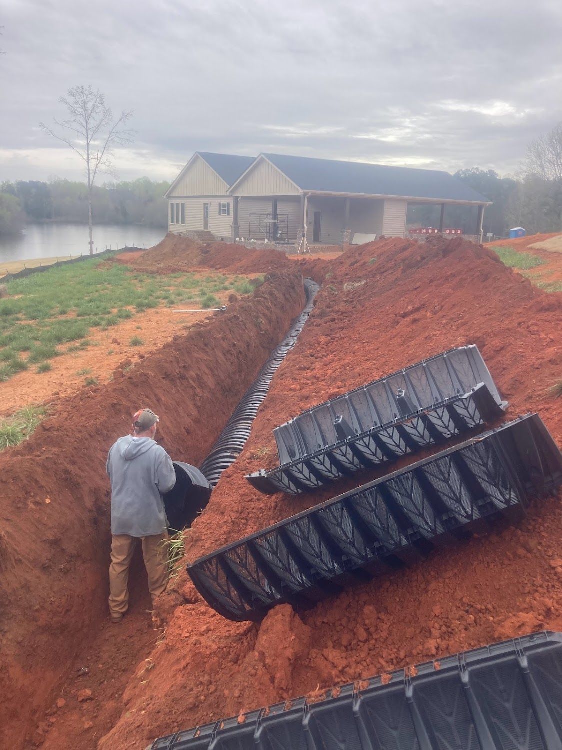 A man is standing in a trench next to a large pile of dirt.