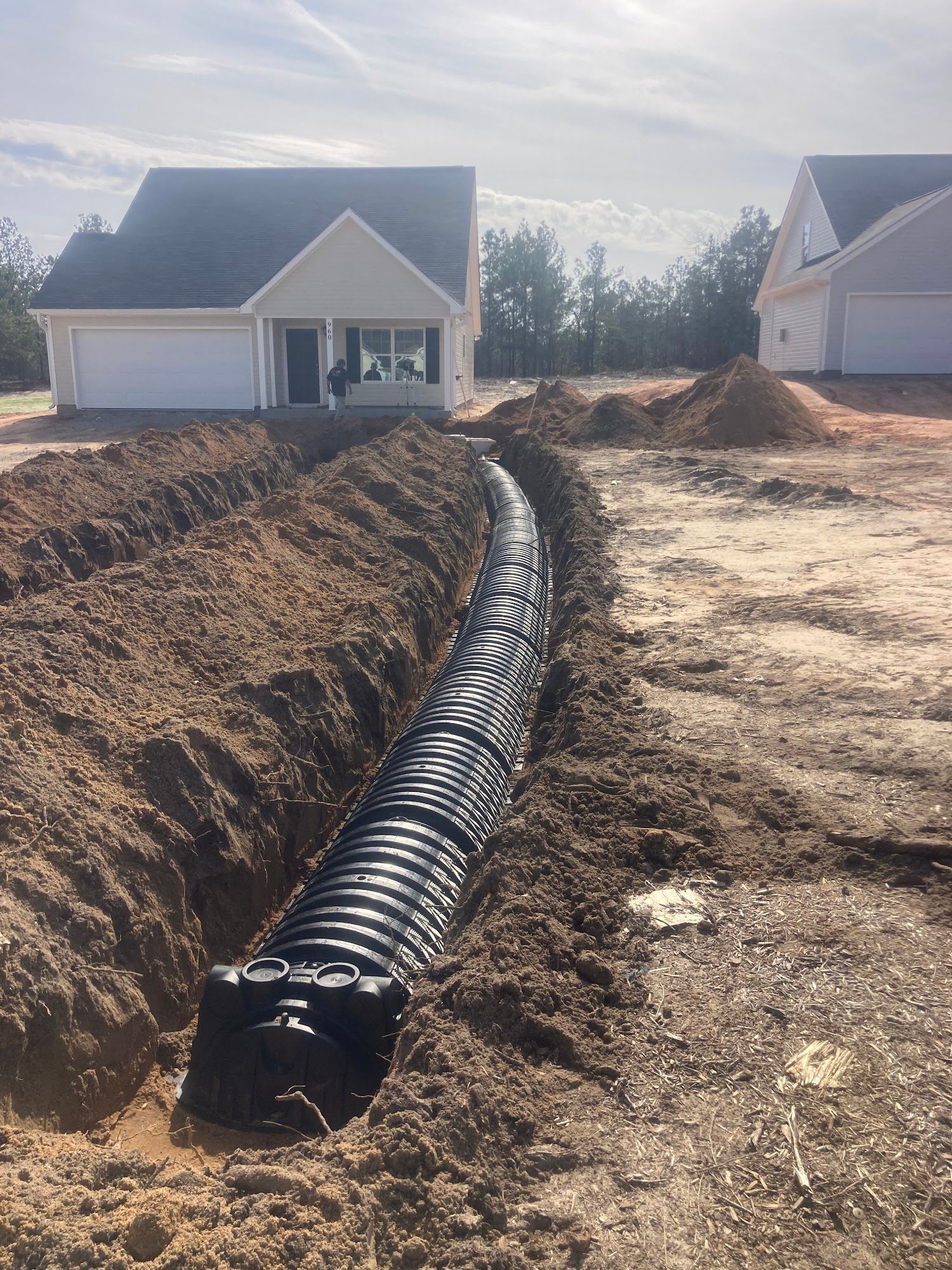 A large pipe is being installed in the dirt in front of a house.