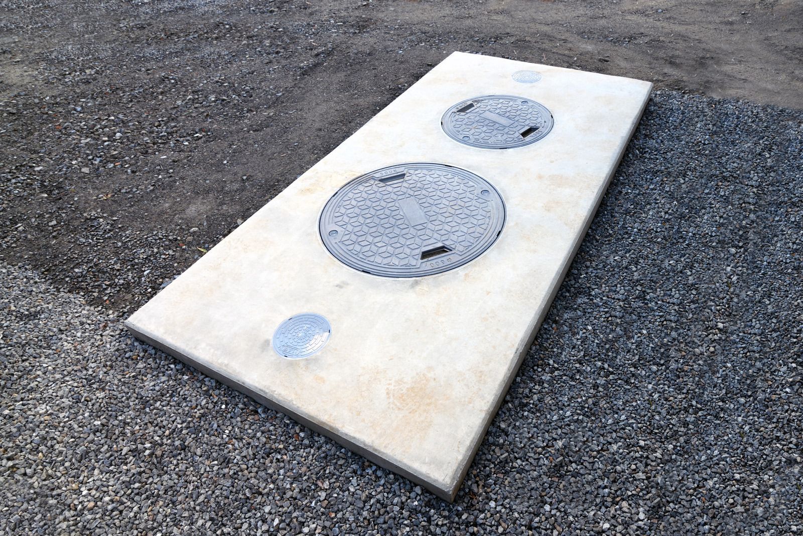 A concrete slab with two manhole covers on it is sitting on top of gravel.
