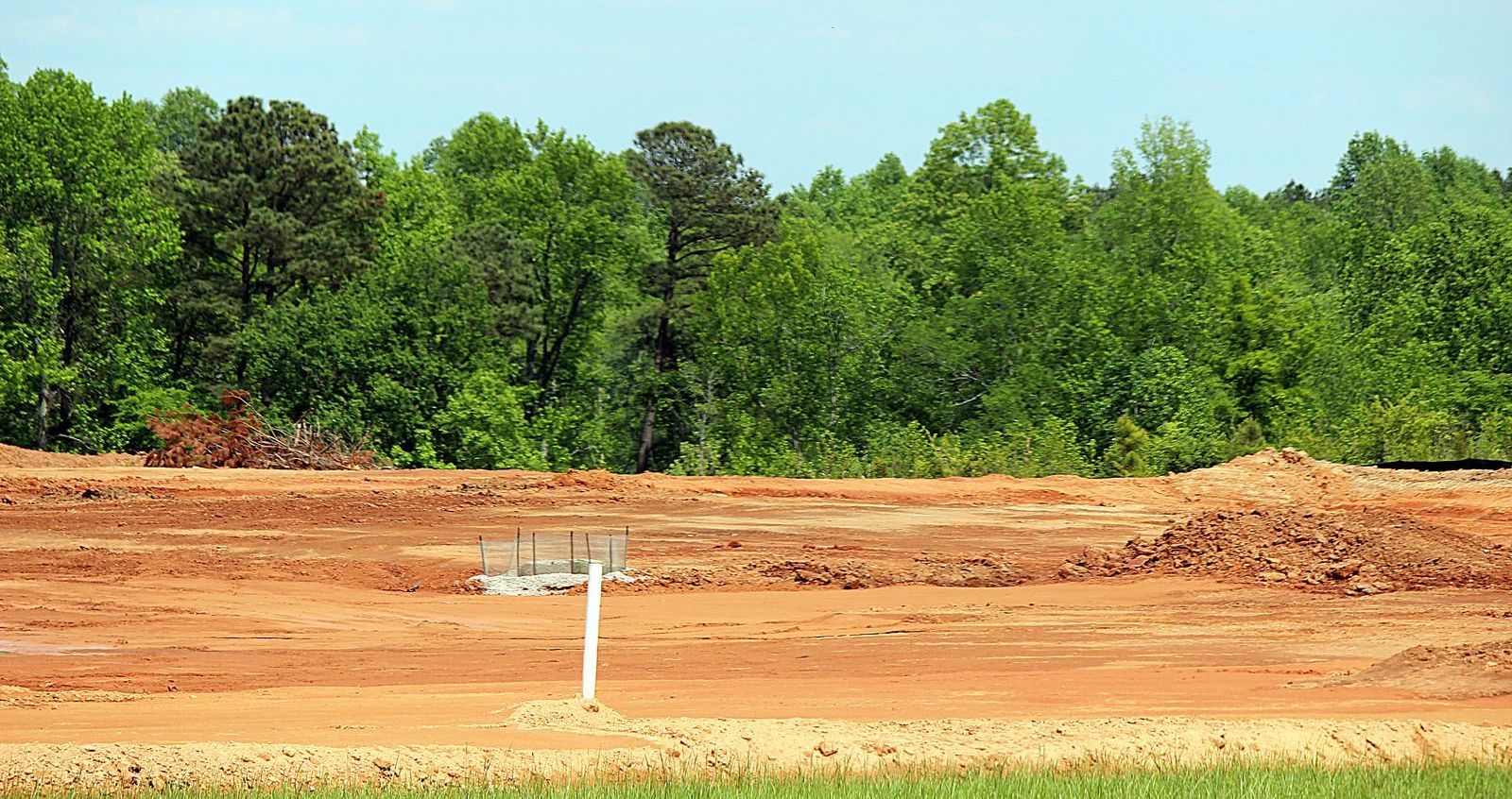 A dirt field with trees in the background and a white pole in the middle.