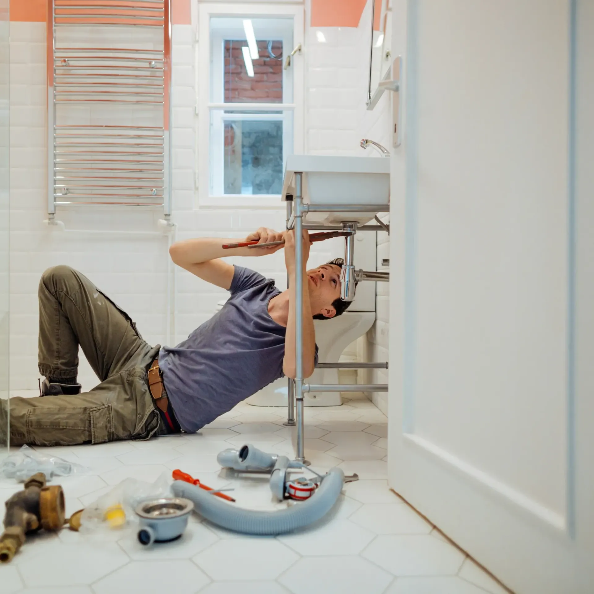 Replacementzone Plumbing - A man is laying on the floor fixing a sink in a bathroom. II