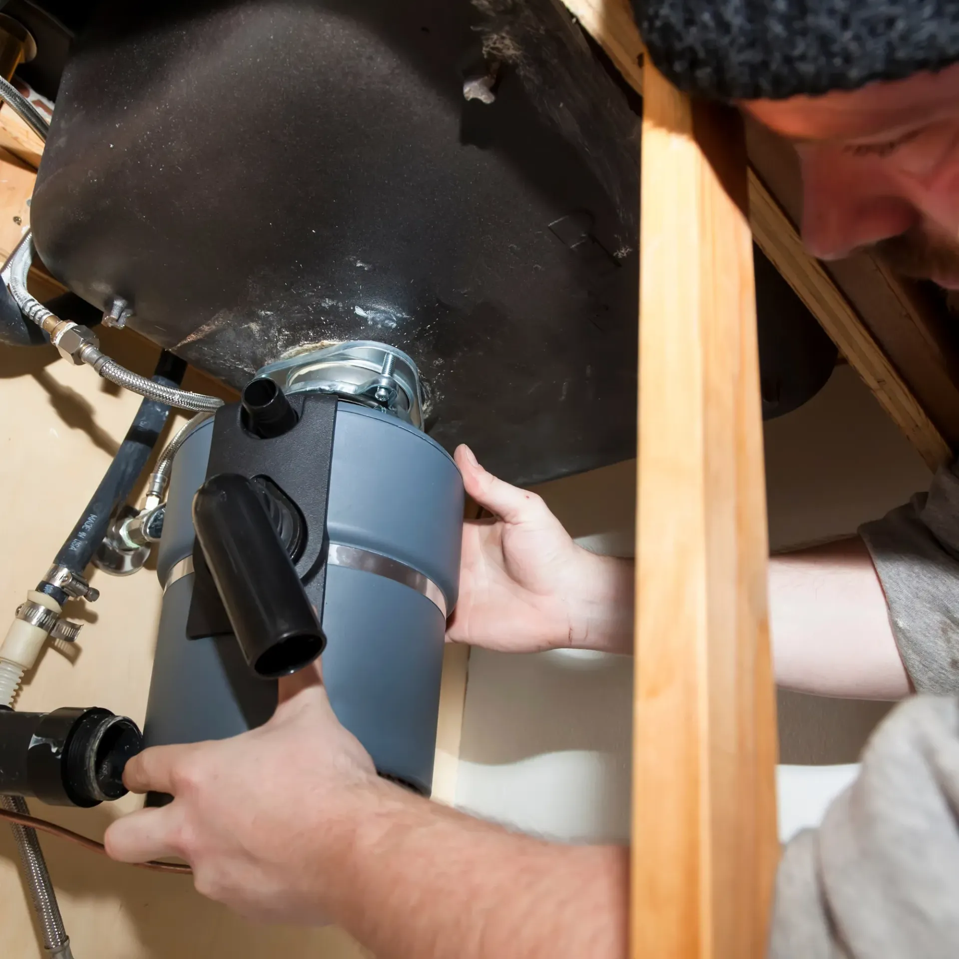 Replacementzone Plumbing - A man is fixing a garbage disposal under a sink II