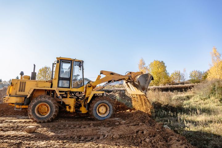 Yellow front loader digging dirt at a muddy construction site under a clear sky