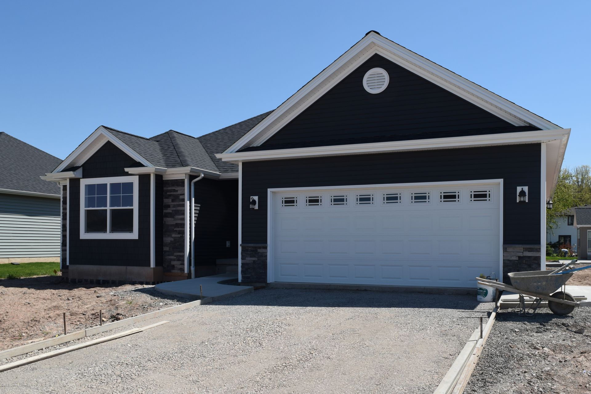 Single-story dark-blue house with white trim, a two-car garage, and a gravel driveway under a clear sky