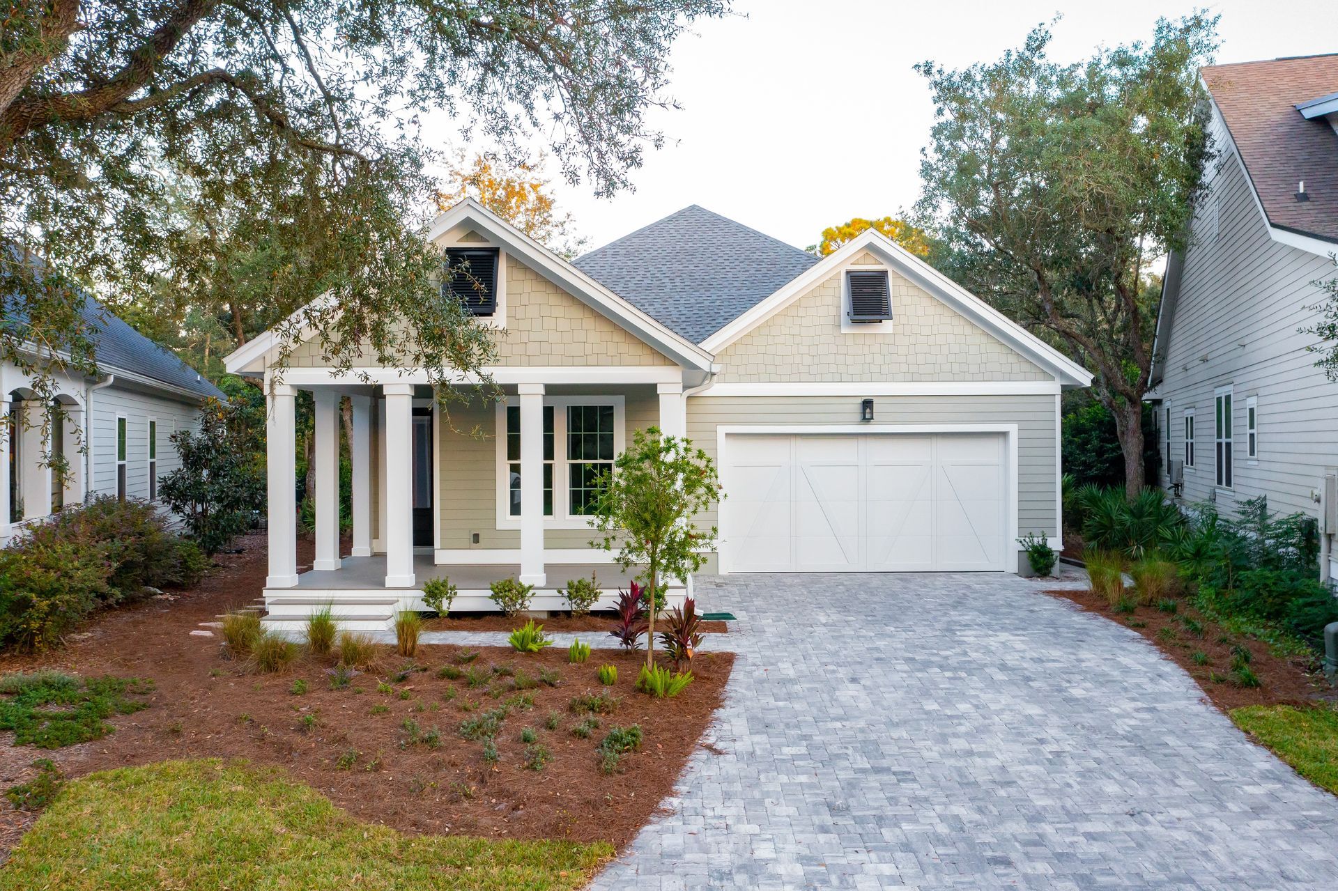 Single-story white house with front porch, white garage, and gray driveway surrounded by landscaping.