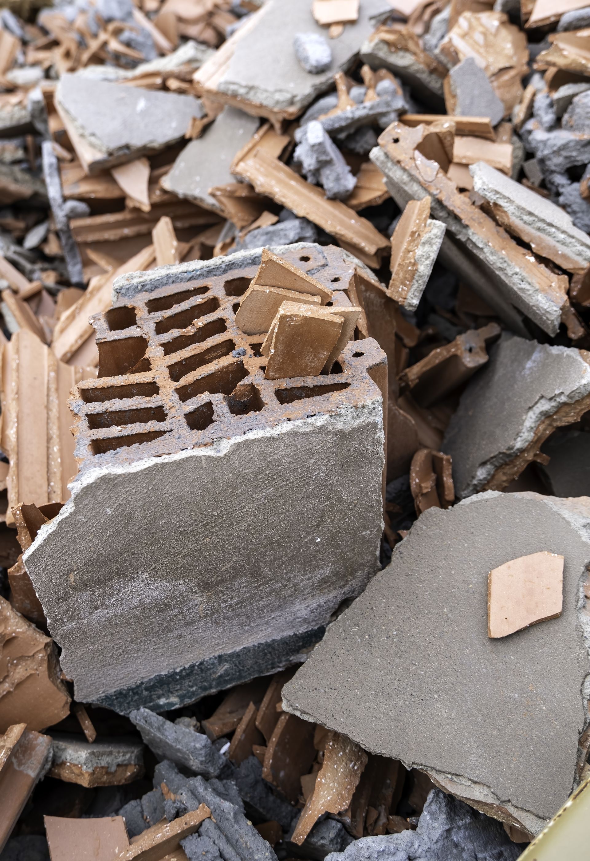 Pile of broken concrete and brick rubble with a gray cinder block fragment and wood debris