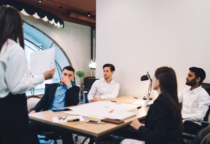 A woman is giving a presentation to a group of people sitting around a table.