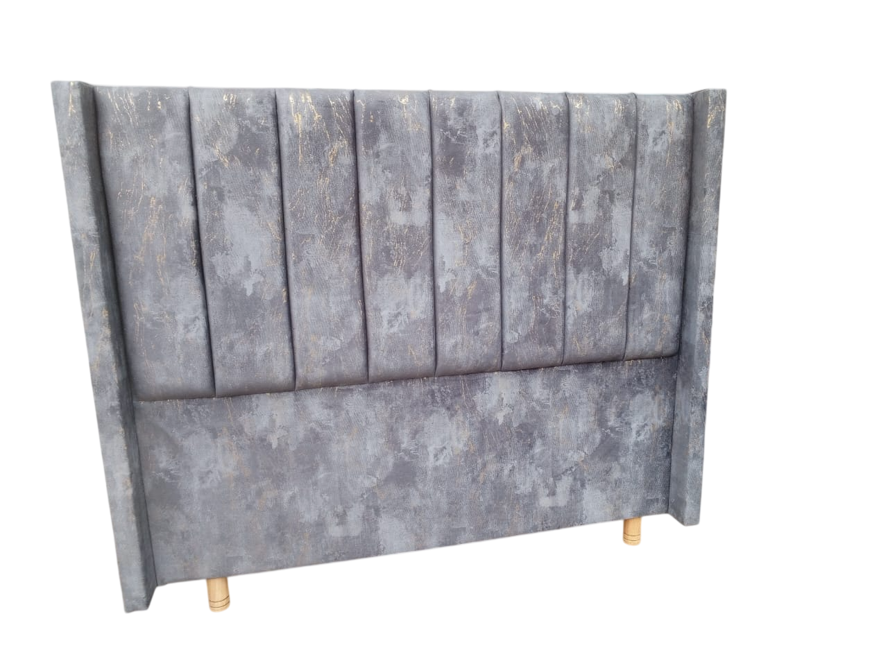 Cabecero tapizado en gris con paneles verticales y patas doradas.