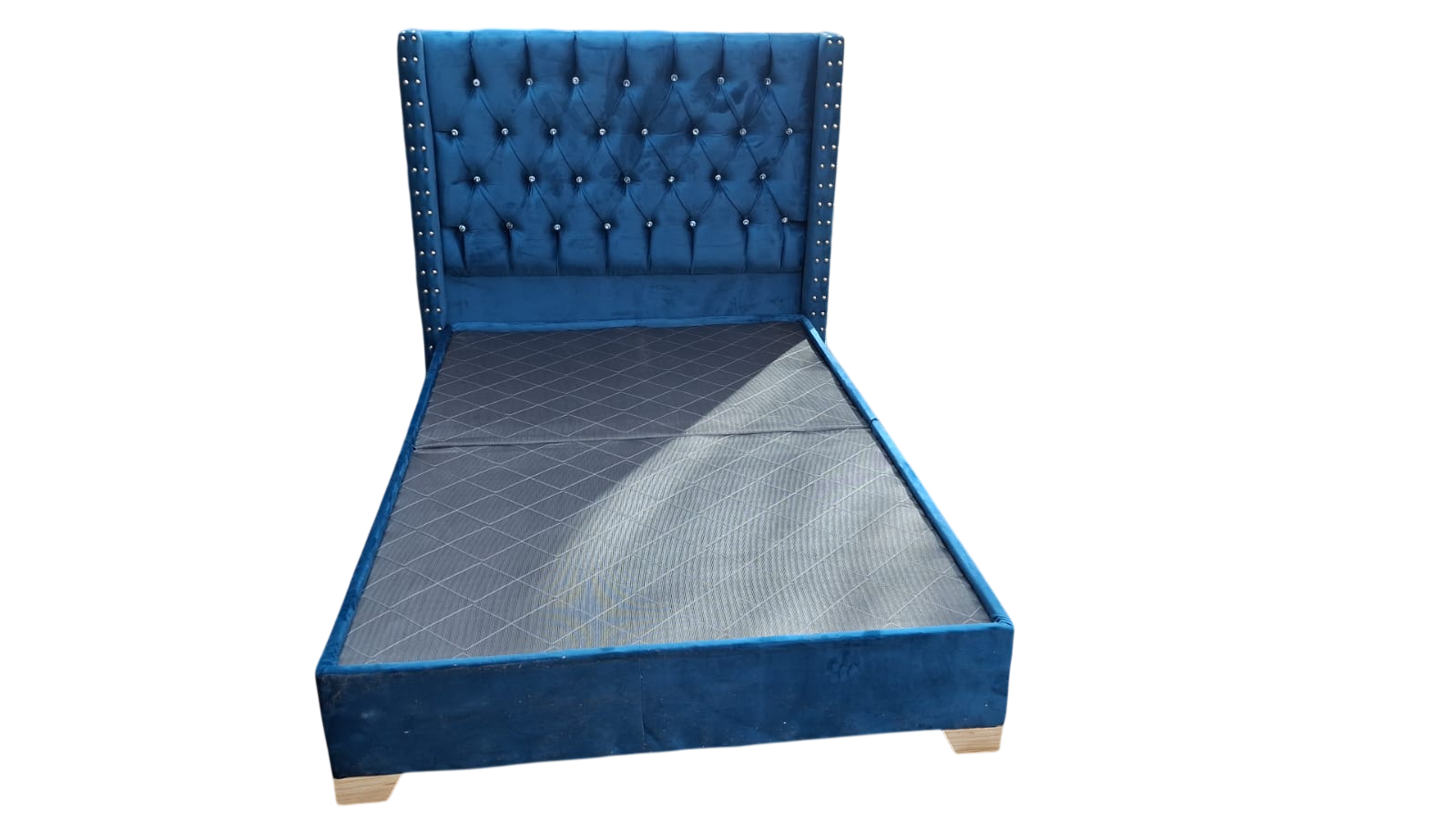 Cama individual tapizada en azul con cabecero capitoné y patas de madera sobre fondo blanco.