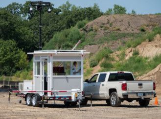 White pickup truck towing a mobile observation booth on a trailer at an outdoor site.