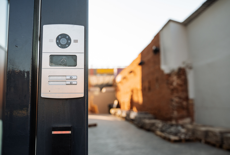 Intercom system on black post, leading into a courtyard with brick building.