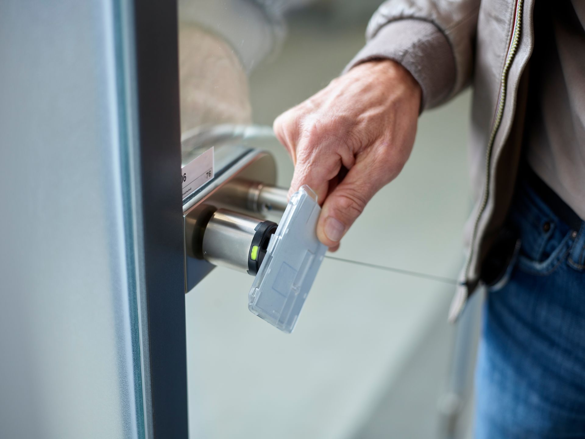 Person swiping a card to unlock a door. Hand holds gray card near a metal access panel.