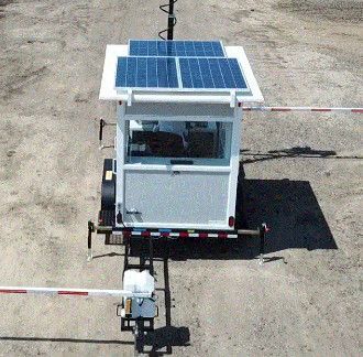 Mobile security booth with solar panels and barrier arms on a gravel surface.