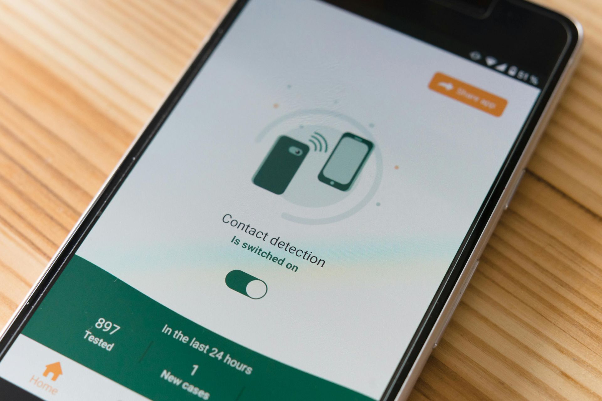 Smartphone displaying contact detection app. Shows connected phones icon and app data on wooden surface.