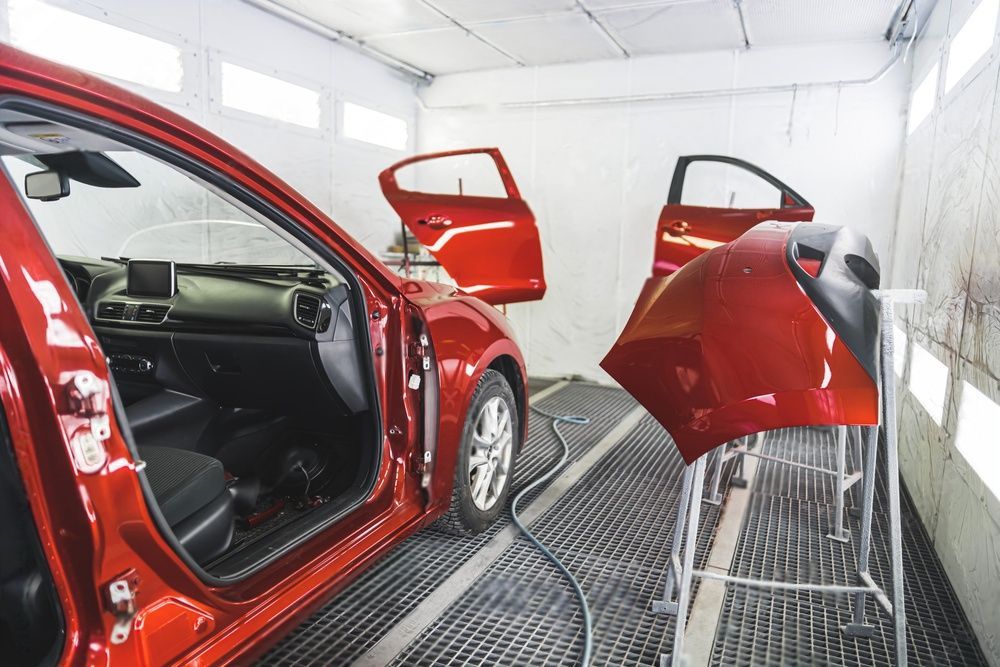 Een rode auto wordt in een spuitcabine gespoten.