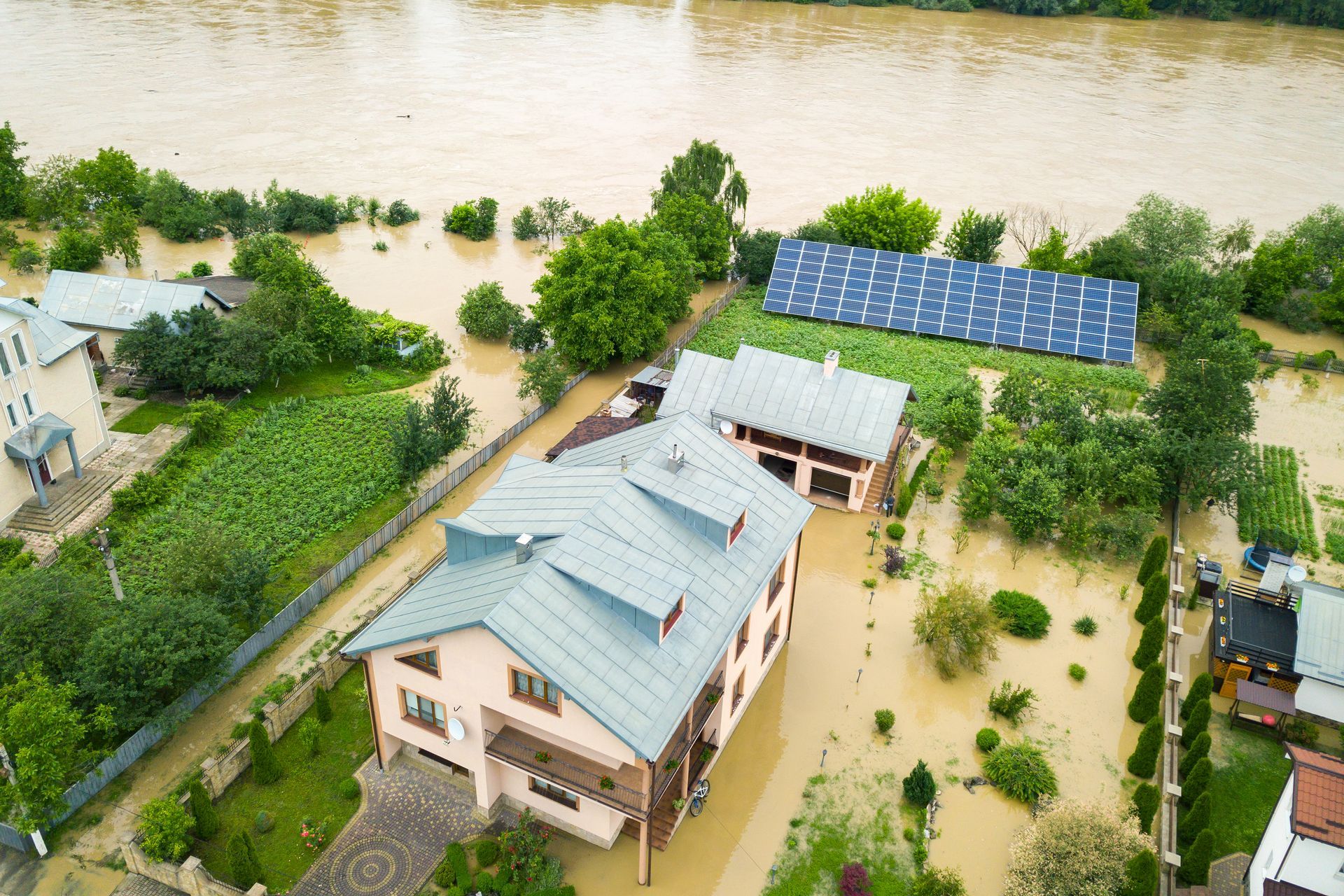 Aerial view of a house surrounded by murky floodwater with solar panels in the yard.