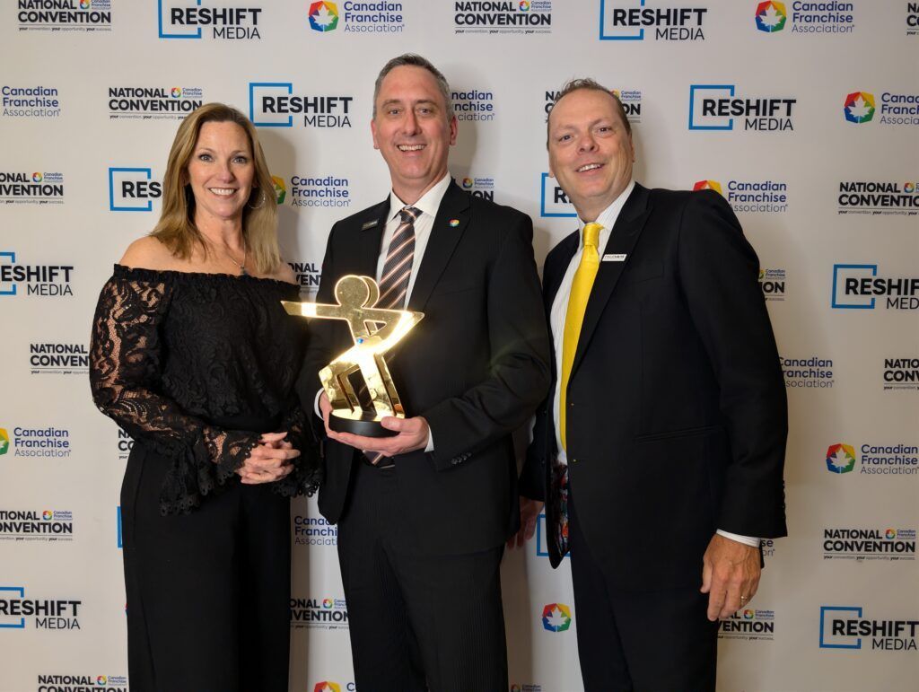 Three people posing with a trophy at a RESHIFT event backdrop