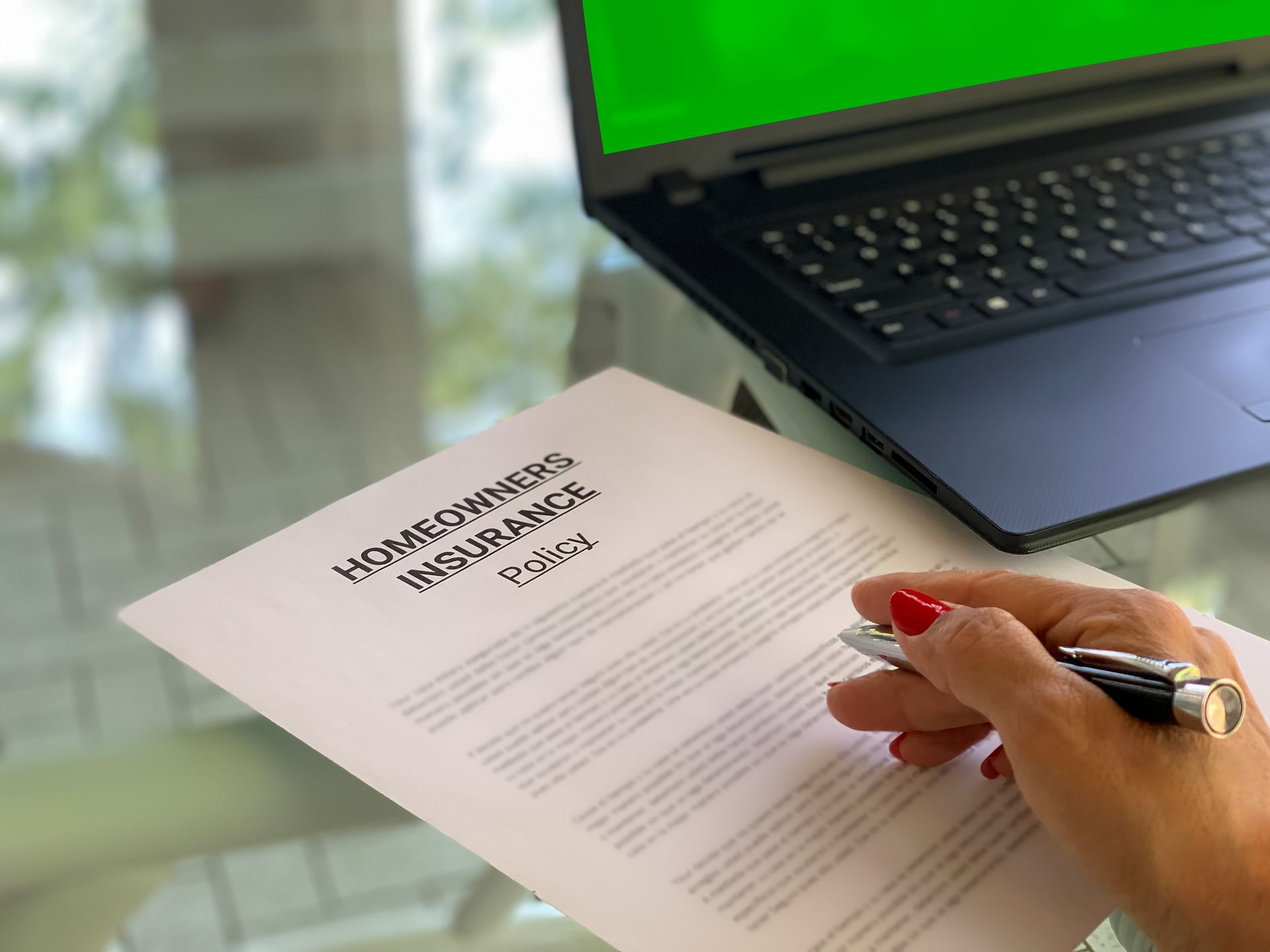 Femme examinant une police d’assurance habitation avec un stylo, près d’un ordinateur portable ouvert.