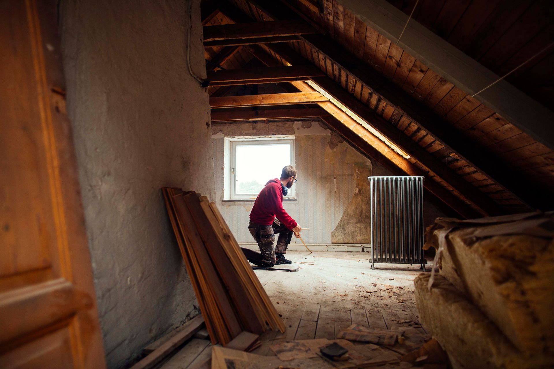 Man inspecting attic near window with tape measure, checking for repairs or winter insulation upgrades.