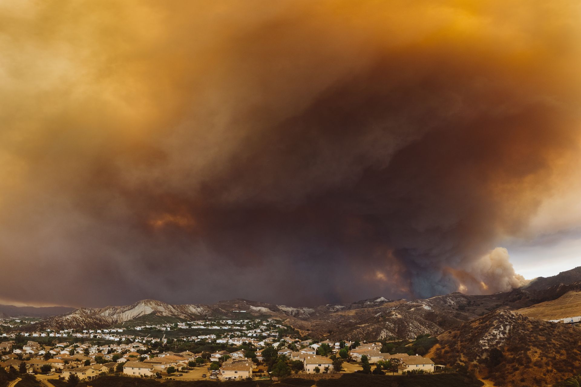 Wildfire smoke clouds darkening an orange sky over a suburban neighbourhood in a valley