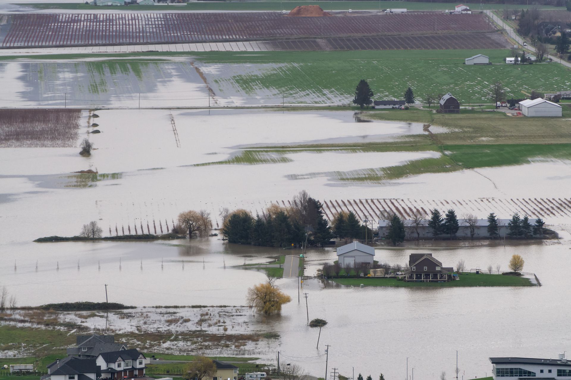 Eau de crue entourant des bâtiments ruraux et des champs après une inondation, route vers une maison