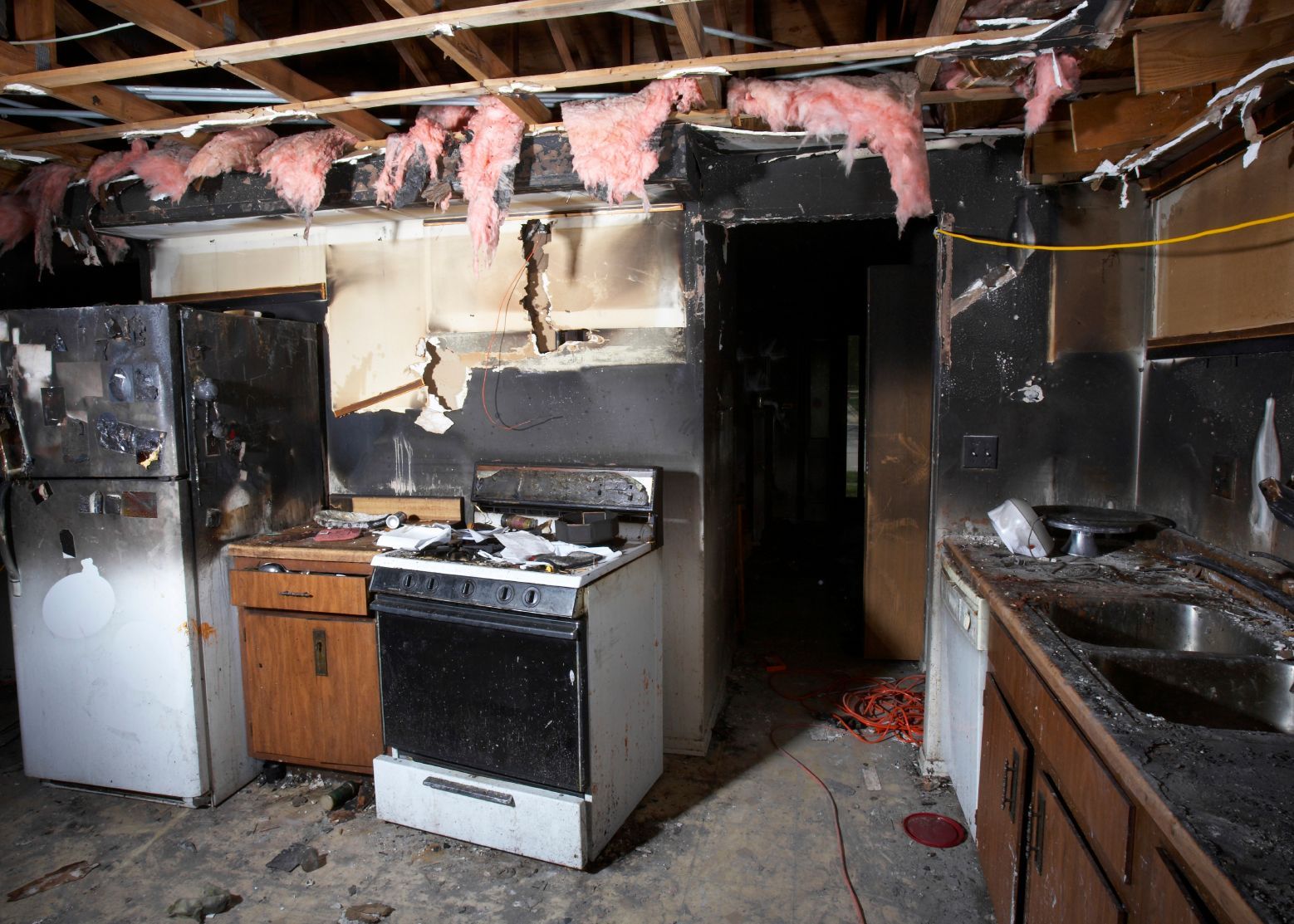 Fire-damaged kitchen with charred ceiling, damaged stove, and smoke-stained cabinets and sink