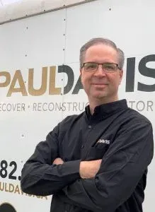 Man in black shirt with glasses, arms crossed in front of a Paul Davis sign.